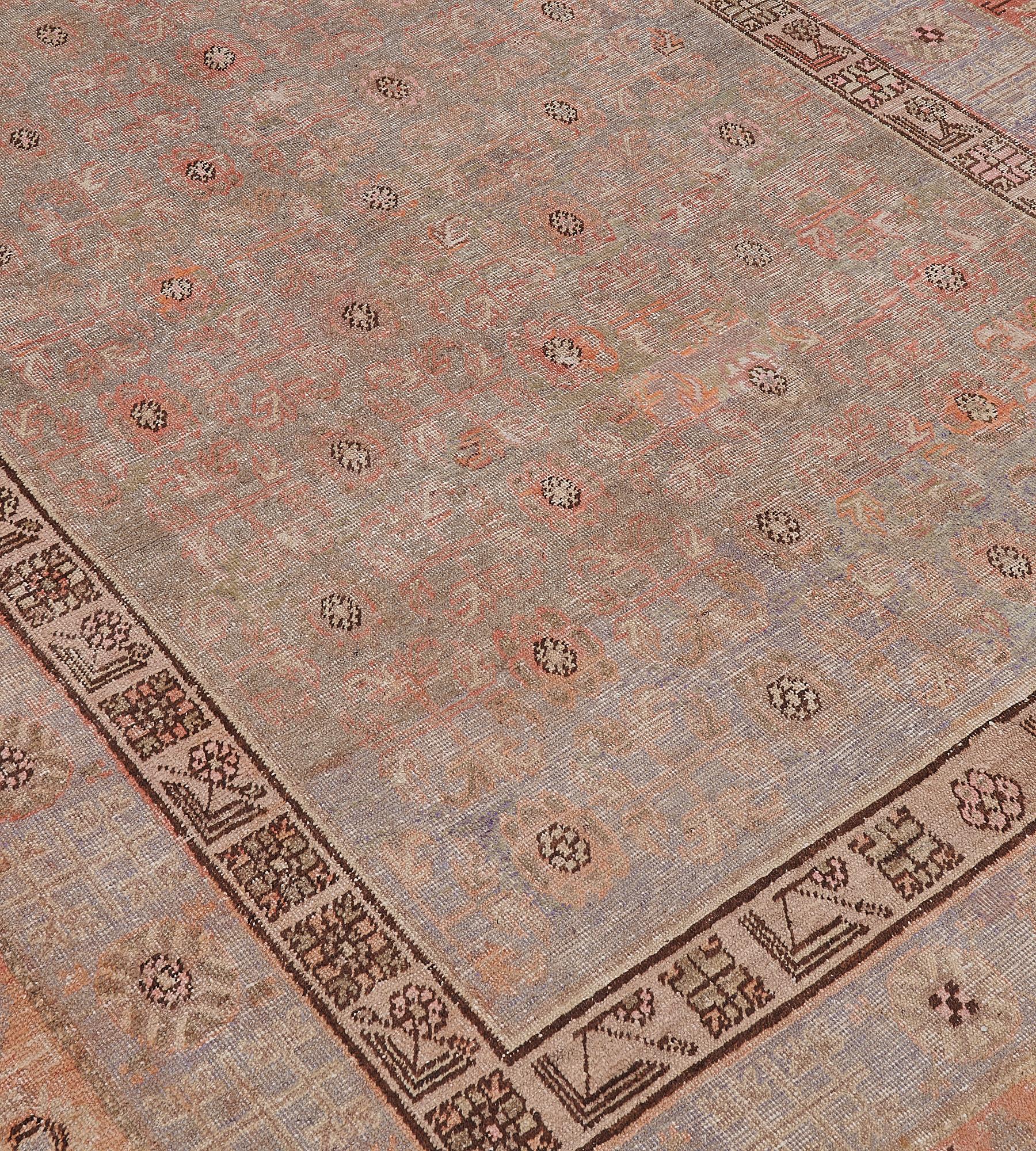 Ce tapis Khotan ancien, vers 1880, a un champ gris pâle avec un motif général de losanges abricot et brun taupe doux et de grands panneaux ouverts à losanges crochetés, dans une bordure gris pâle de palmettes brun taupe alternant avec des motifs