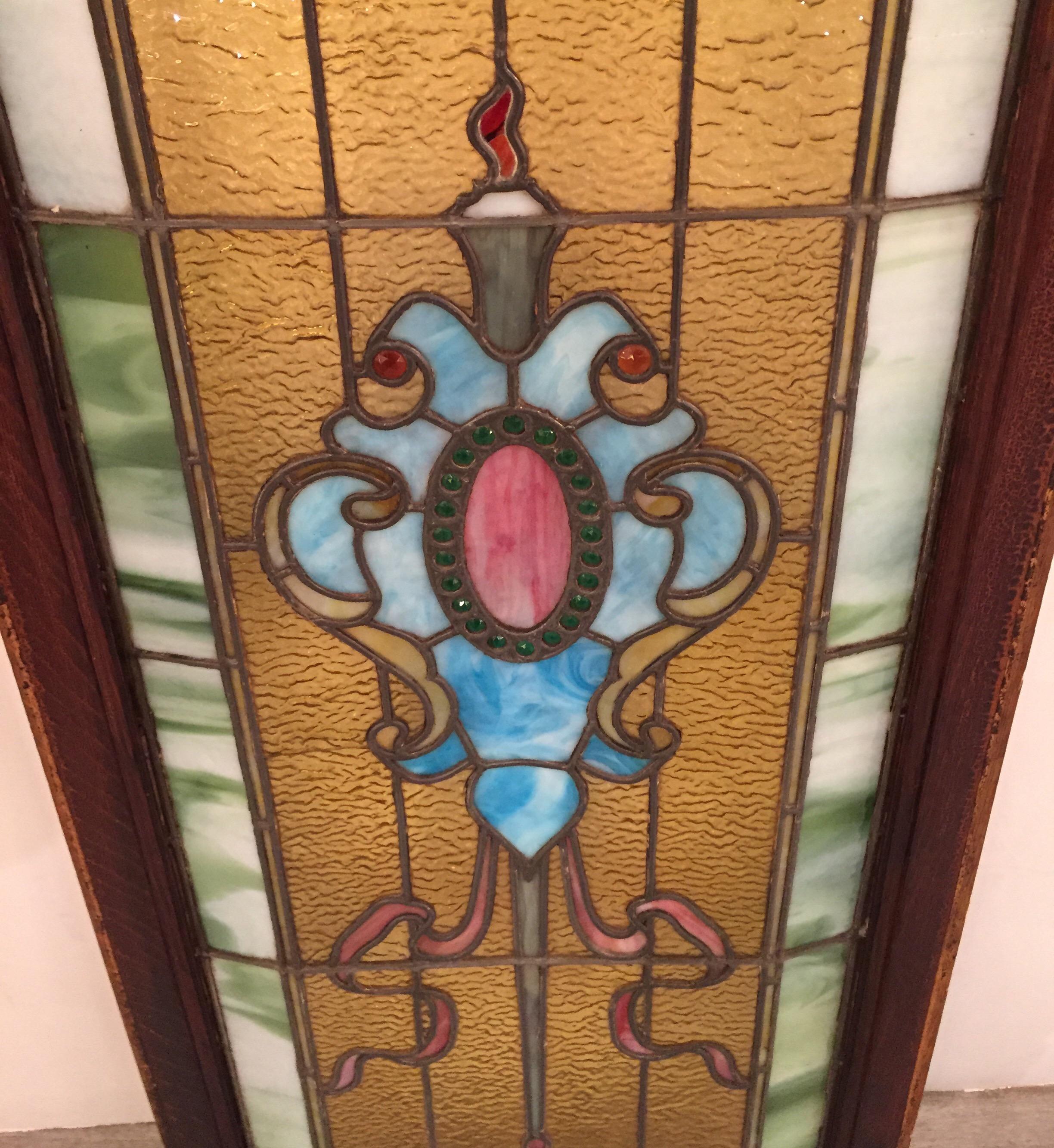 Original 19th century stained glass panel with wood frame. The shield pattern centered flanked by ribbons with an amber background. The outside edge with a green marbleized border. One small panel of glass with a slight crack. The entire stained