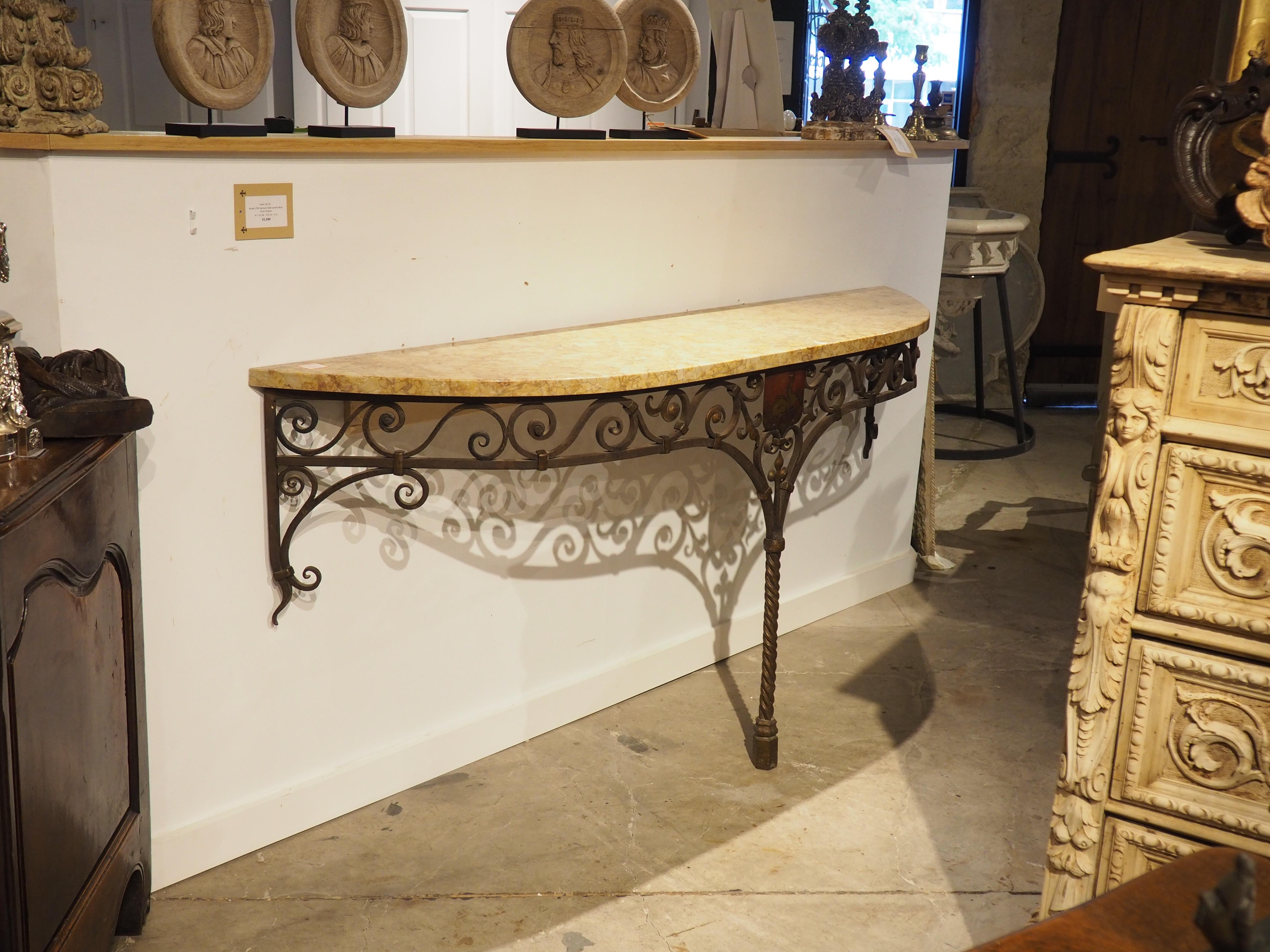 Embellished by a painted coat of arms placard, set above the single leg, this wrought iron console with marble top dates to circa 1880. The blason is a shaped, red shield with a golden mythical creature surmounting flames and topped by a closed