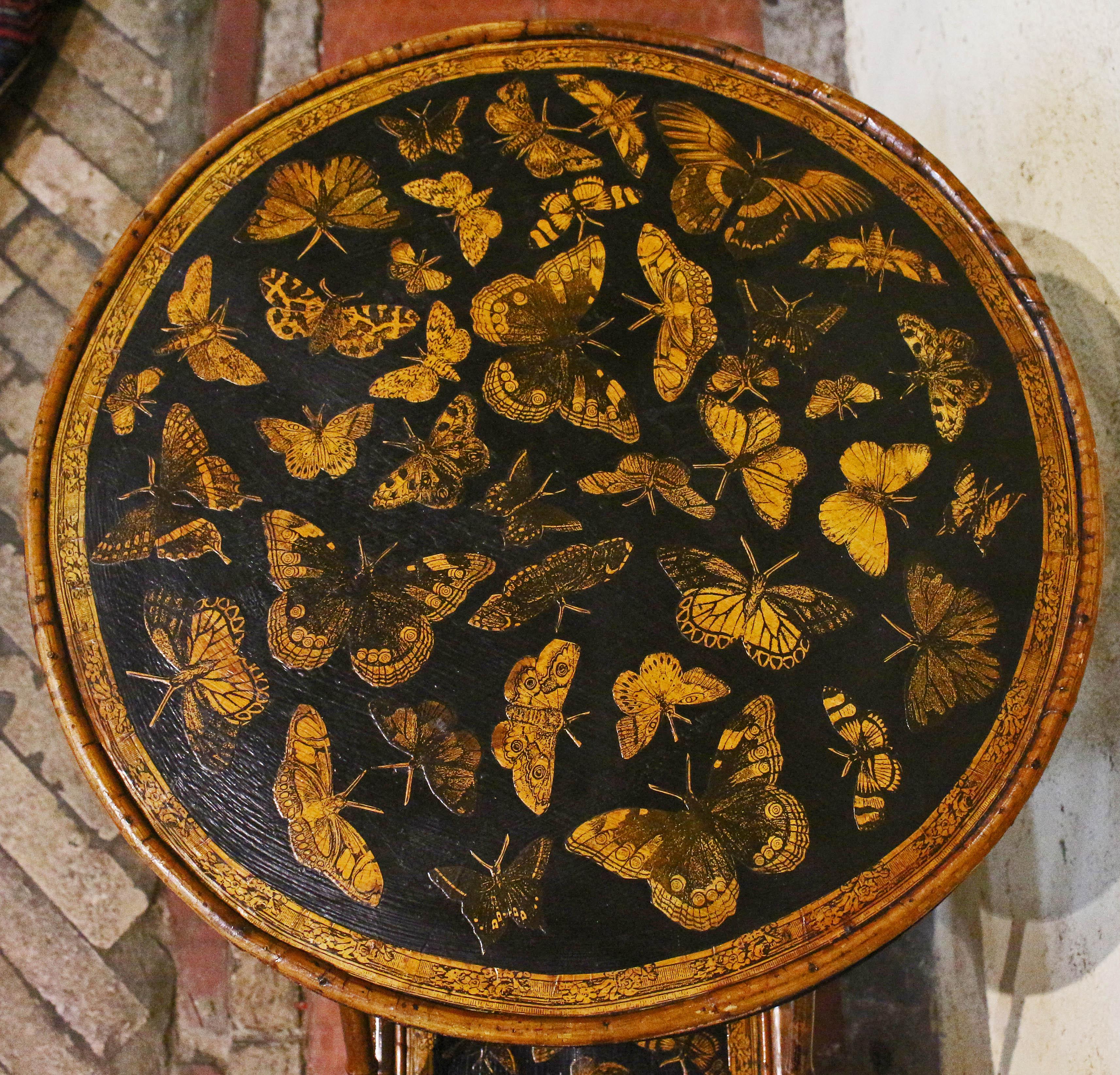 Mesa inglesa de bambú de varios pisos, circa 1880. Ahora las superficies están decoradas artesanalmente con mariposas. Parte superior redonda sobre nivel inferior cuadrado con lados de caída cuadrados. 17 7/8