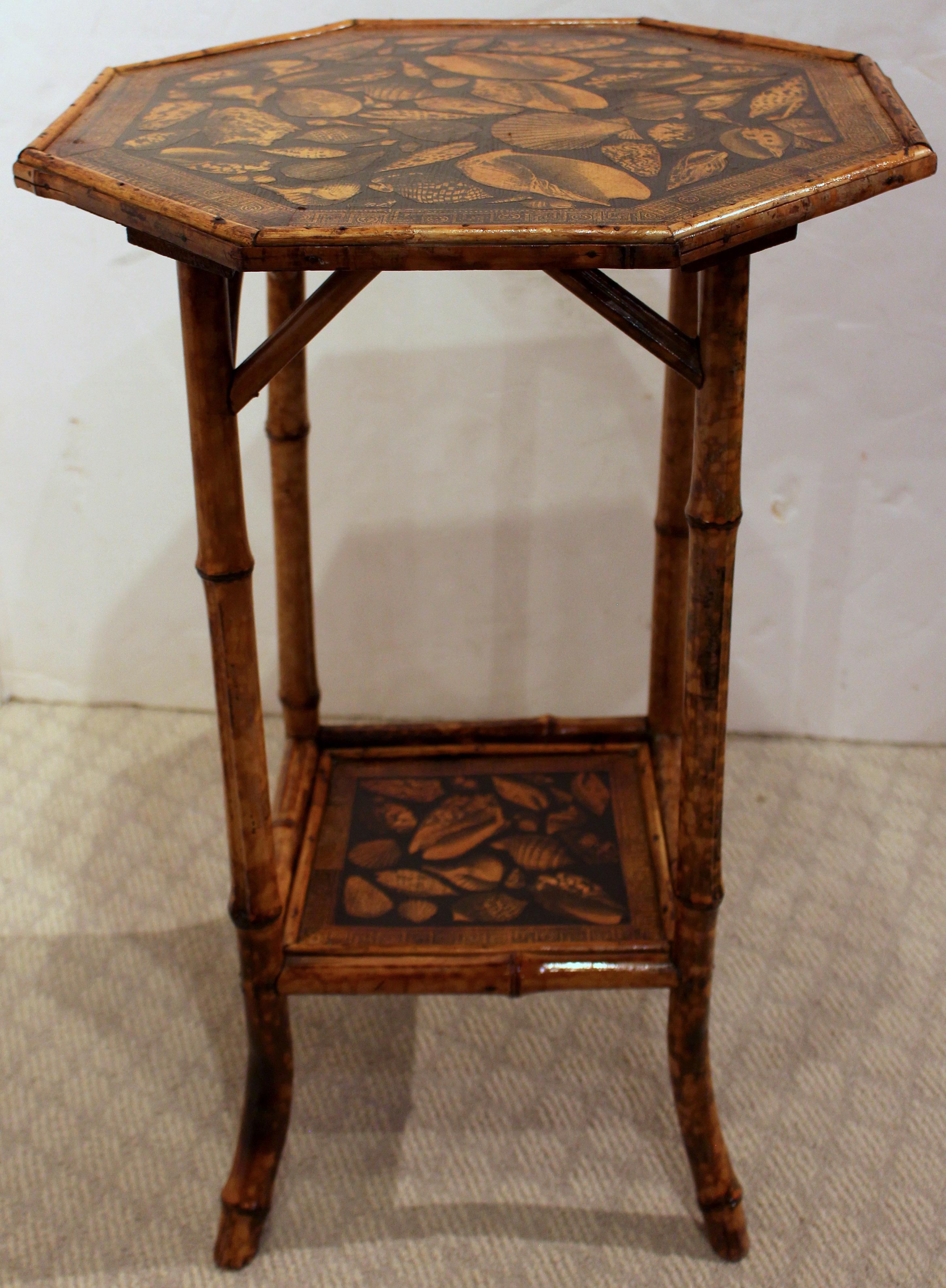 Circa 1880 octagonal top 2-tier bamboo table, English. Architectural struts. The original rattan surfaces now artisan decoupaged with shells. French splay feet.
17 7/8