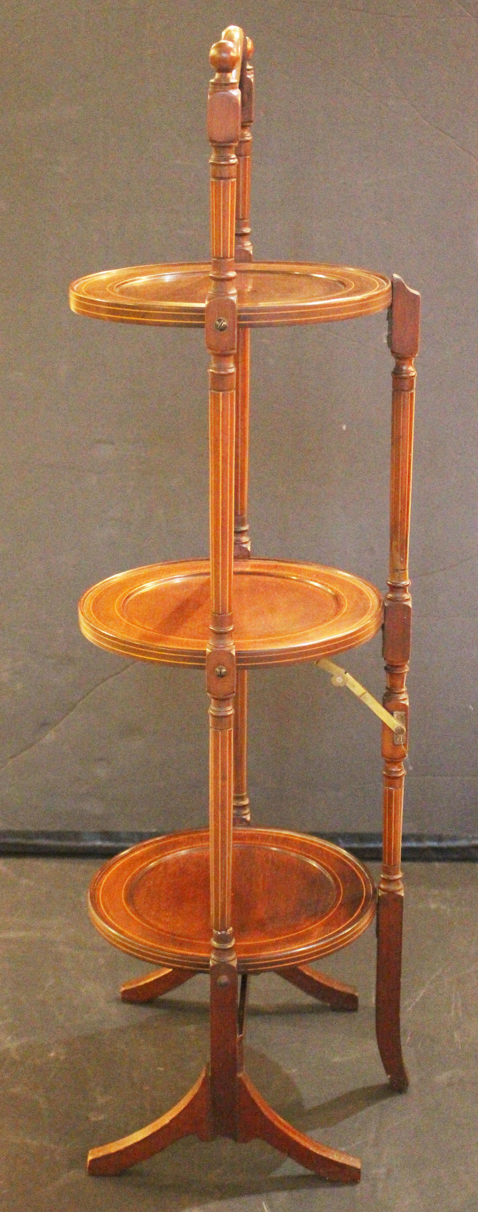 Circa 1885-1905 Sheraton Revival Tilting Muffin Stand, English. Mahogany with boxwood line inlays. Finial topped turned standards with line inlays, raised on splay feet. Shaped top carrying handle. 12
