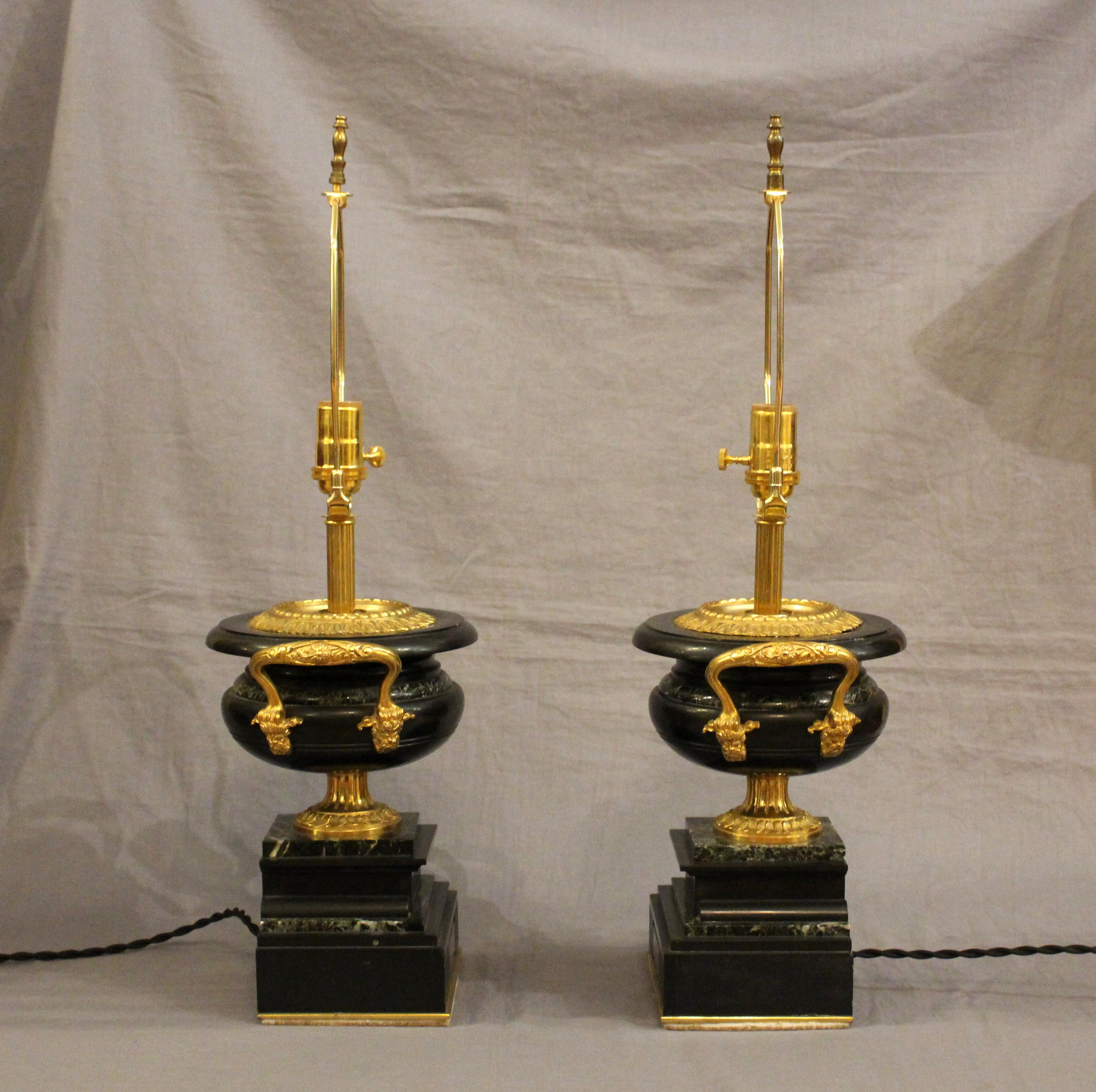 Circa 1890-1910 par de lámparas de sobremesa urna de mármol y bronce dorado, inglesas. Creado a partir de guarniciones del manto. El negro y el negro con venas blancas se alternan en las formas campana. Monturas de bronce dorado. Astillas muy