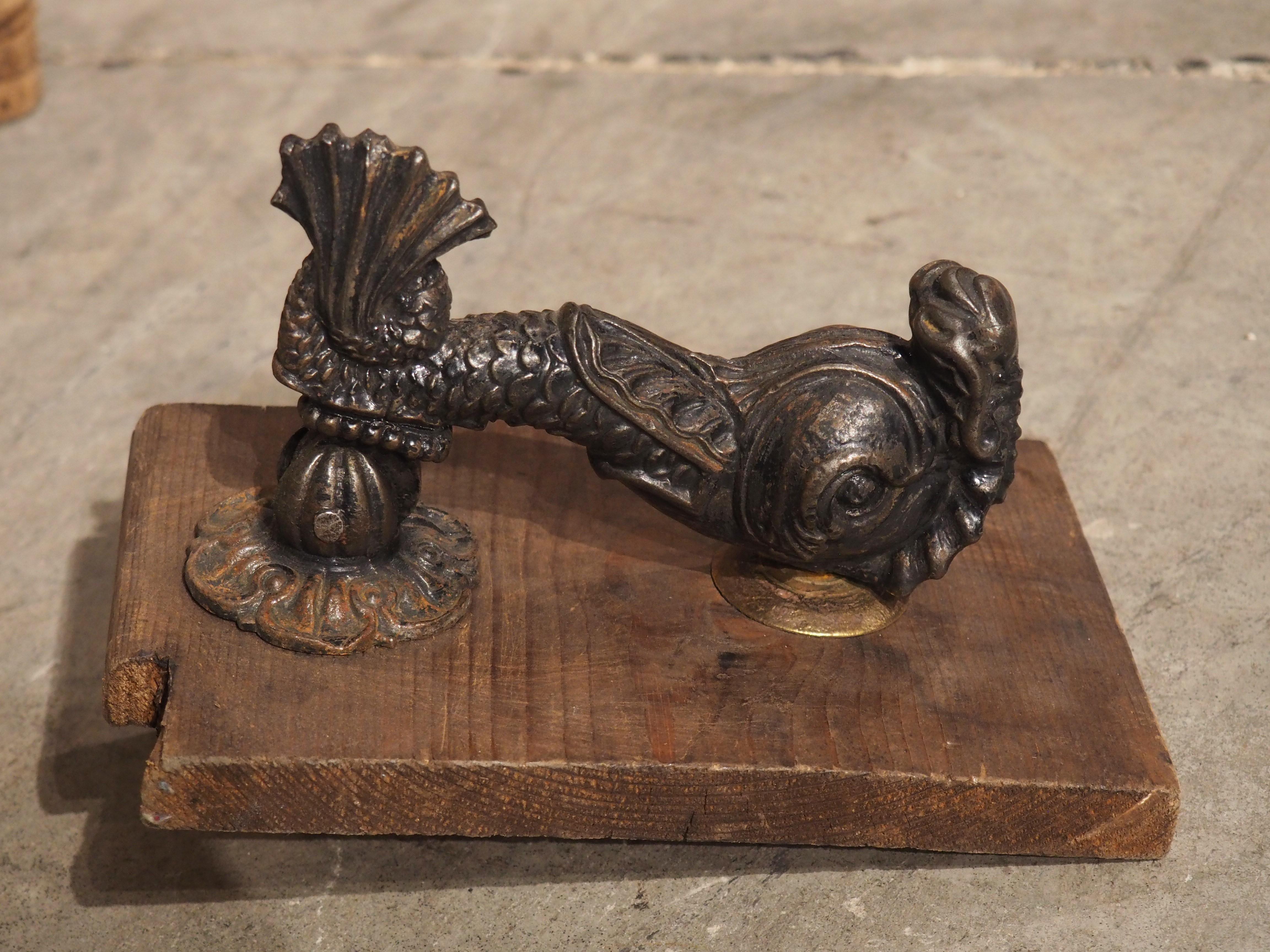 Produced in France, circa 1890, this cast iron door knocker is in the form of a French dolphin. The volute tail of the dolphin is affixed to a divided leaf mount with beading filling the parts. A circular strike plate, which is most likely not