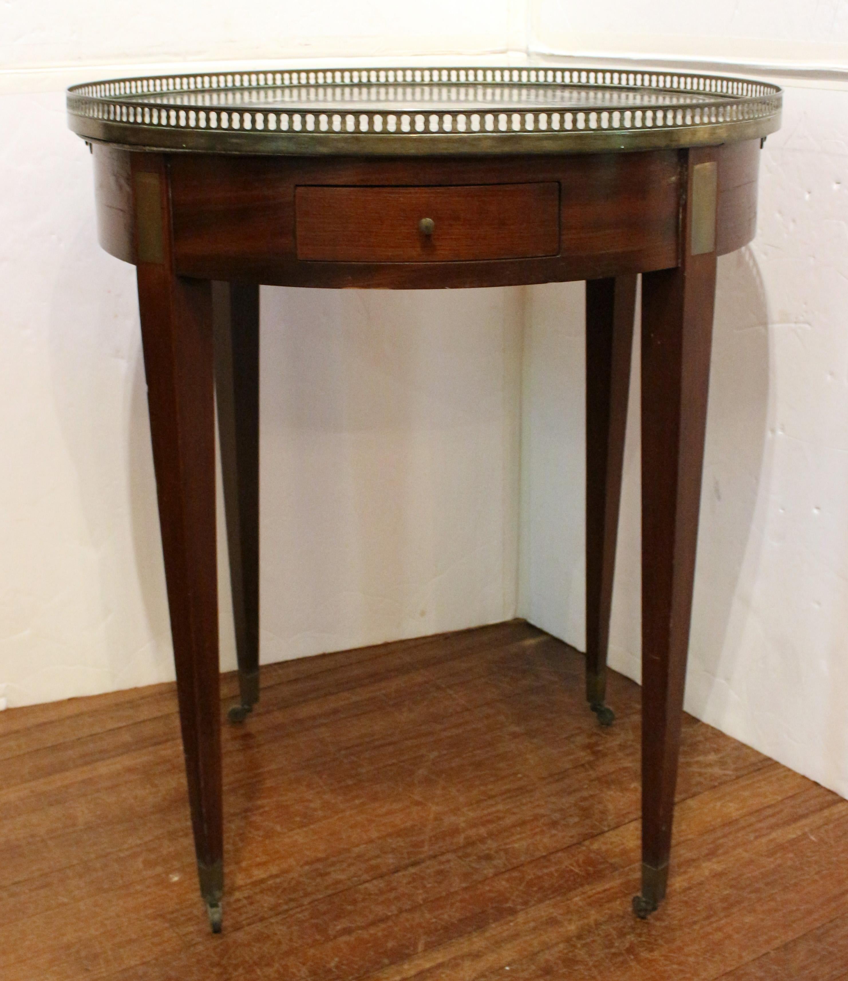 Circa 1890 marble top bouillotte table, Louis XVI style, French. Mahogany with straight, tapered legs ending in sabots & casters. Grey marble with white striations. Brass Gallery. Brass rectangular plaque mounts. Opposing drawers & slides. Brass