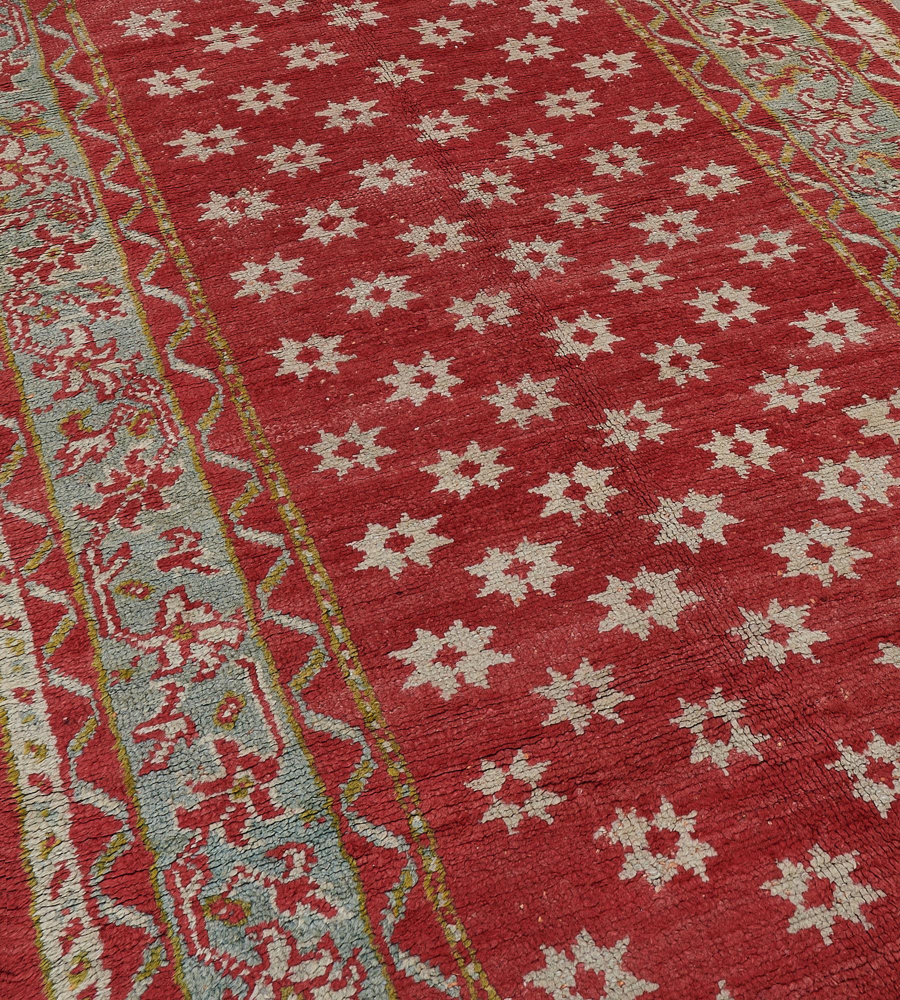 Questo antico runner Oushak, risalente al 1900 circa, ha un campo rosso mattone con file diagonali di teste di fiori stellari blu ghiaccio, in un bordo blu ghiaccio con una vite floreale serpeggiante tra nastro rosso mattone e strisce minori a