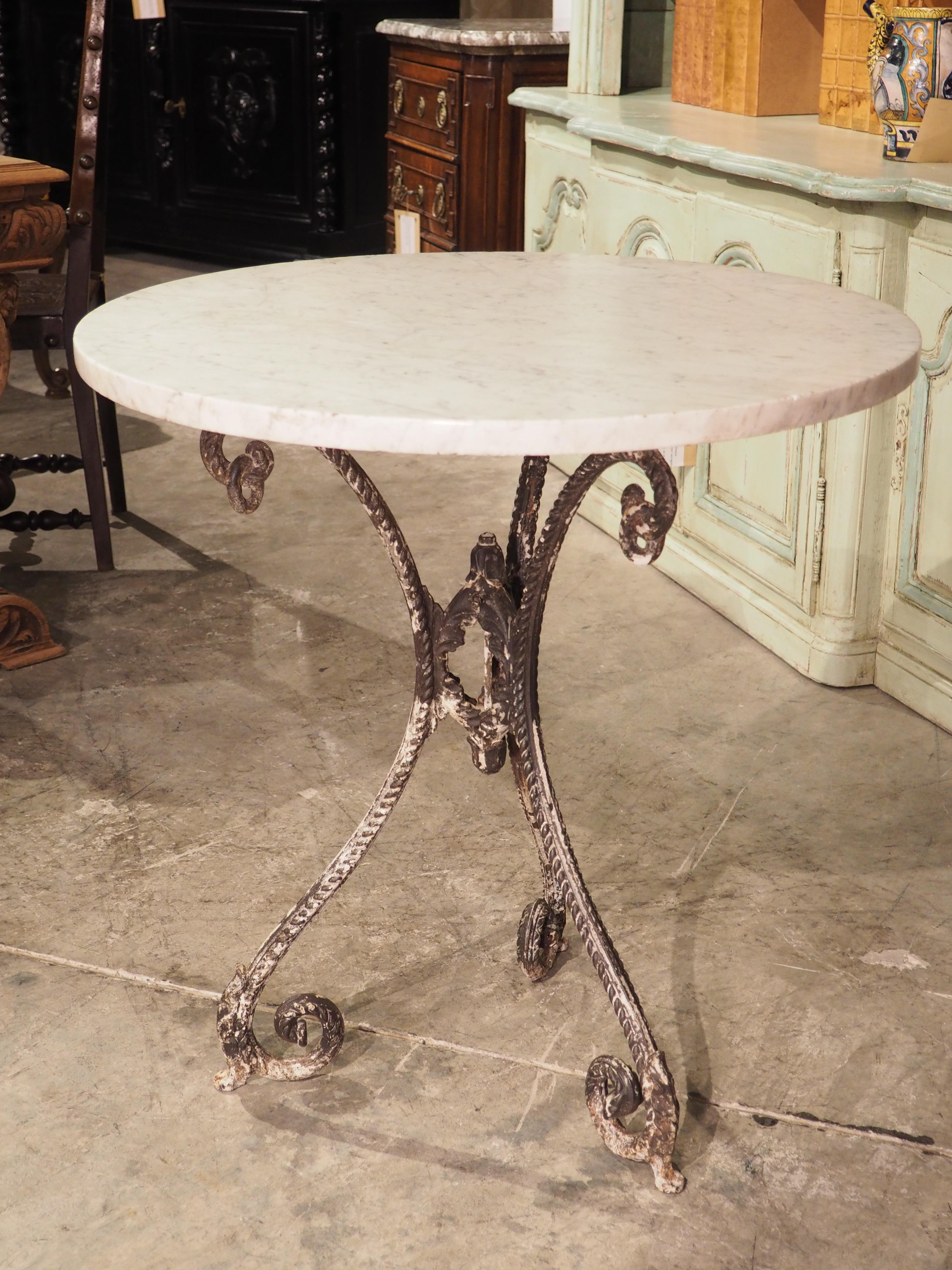 Produced in France, circa 1900, this cast iron and carrara marble bistro table can comfortably sit two people. The round top is white with gray veining and the tripartite cast iron base has been parcel patinated in a similar color. Each leg is