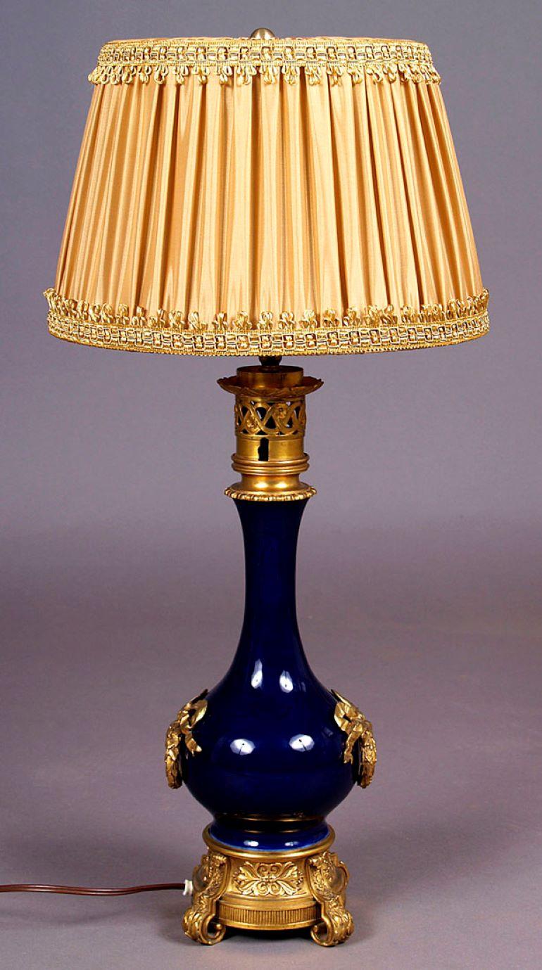 Cobalt porcelain and gilded bronze table lamp, circa 1900
Table lamp, round base with four curved legs and engraved in leaf patterns. Above, a wider belly, narrowed upwards, with decorations made of gilded bronze in the form of laurel wreaths with