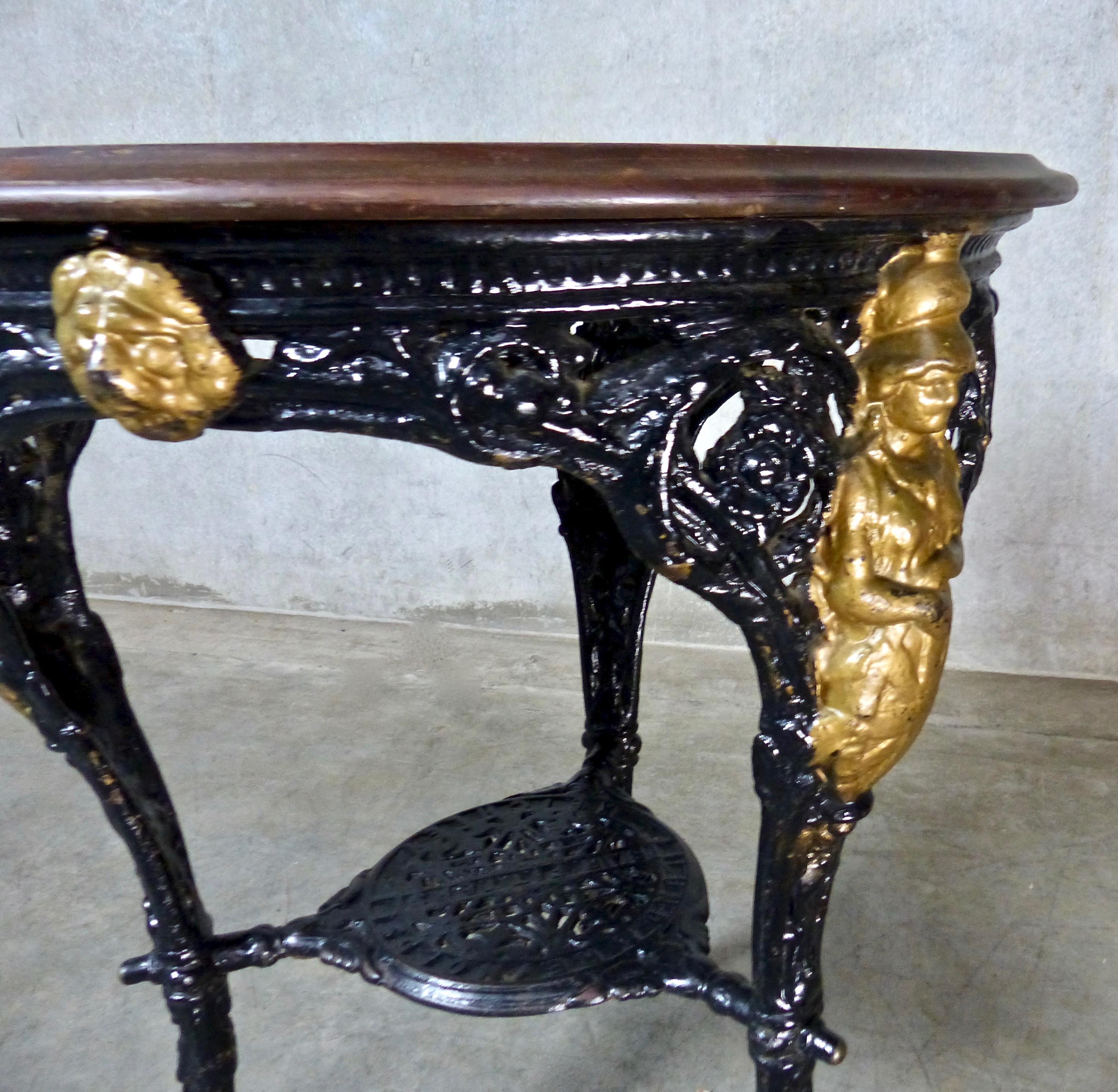 A circa 1900, ornate, three-legged, cast iron round pub table by Lund & Reynolds Ltd. of Bradford, England. Some gilt statuary details, lion’s paw feet, and solid mahogany top. Suitable as a statement-making centre, entry hall, or console