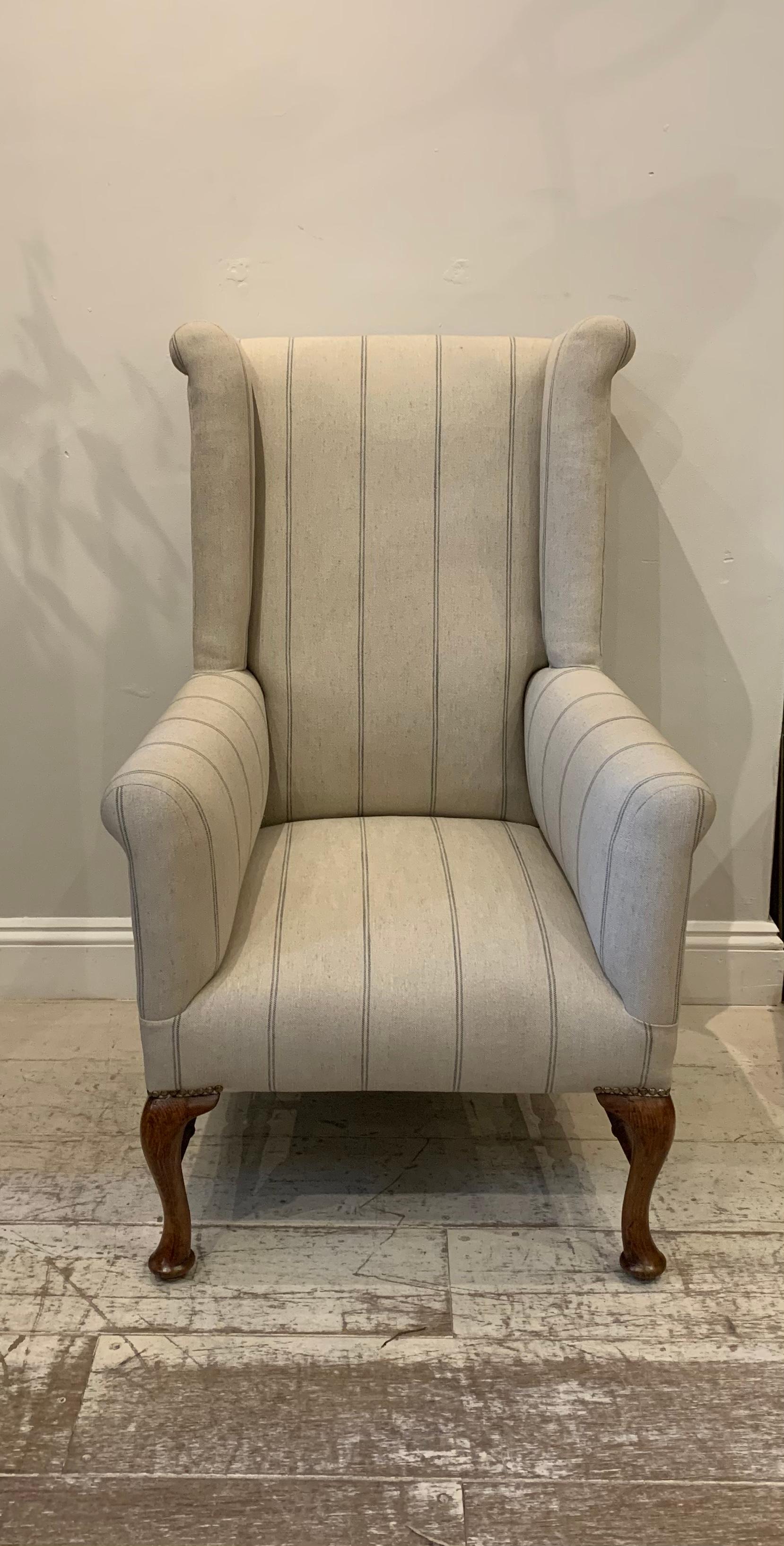 A useful and compact wingback armchair. Circa 1900s and most likely to be English. The armchair has recently been reupholstered in a neutral linen with a fire retardant fabric with blue ticking style stripe running vertically down it.

The legs