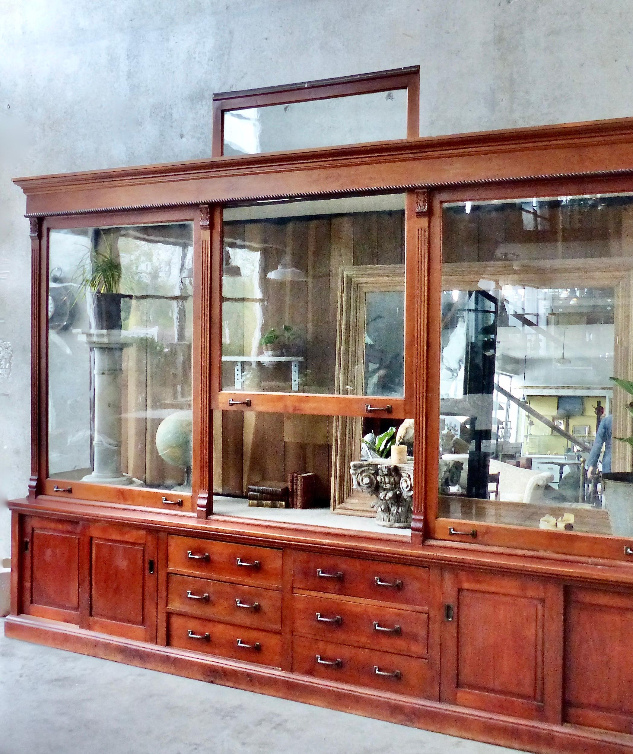 A circa 1900, solid maple store cabinet stained to emulate cherrywood and retaining its original finish. Rare glass front panels that lift upward to open. Columns and barley twist details on the upper portion. Multiple drawers and sliding doors in