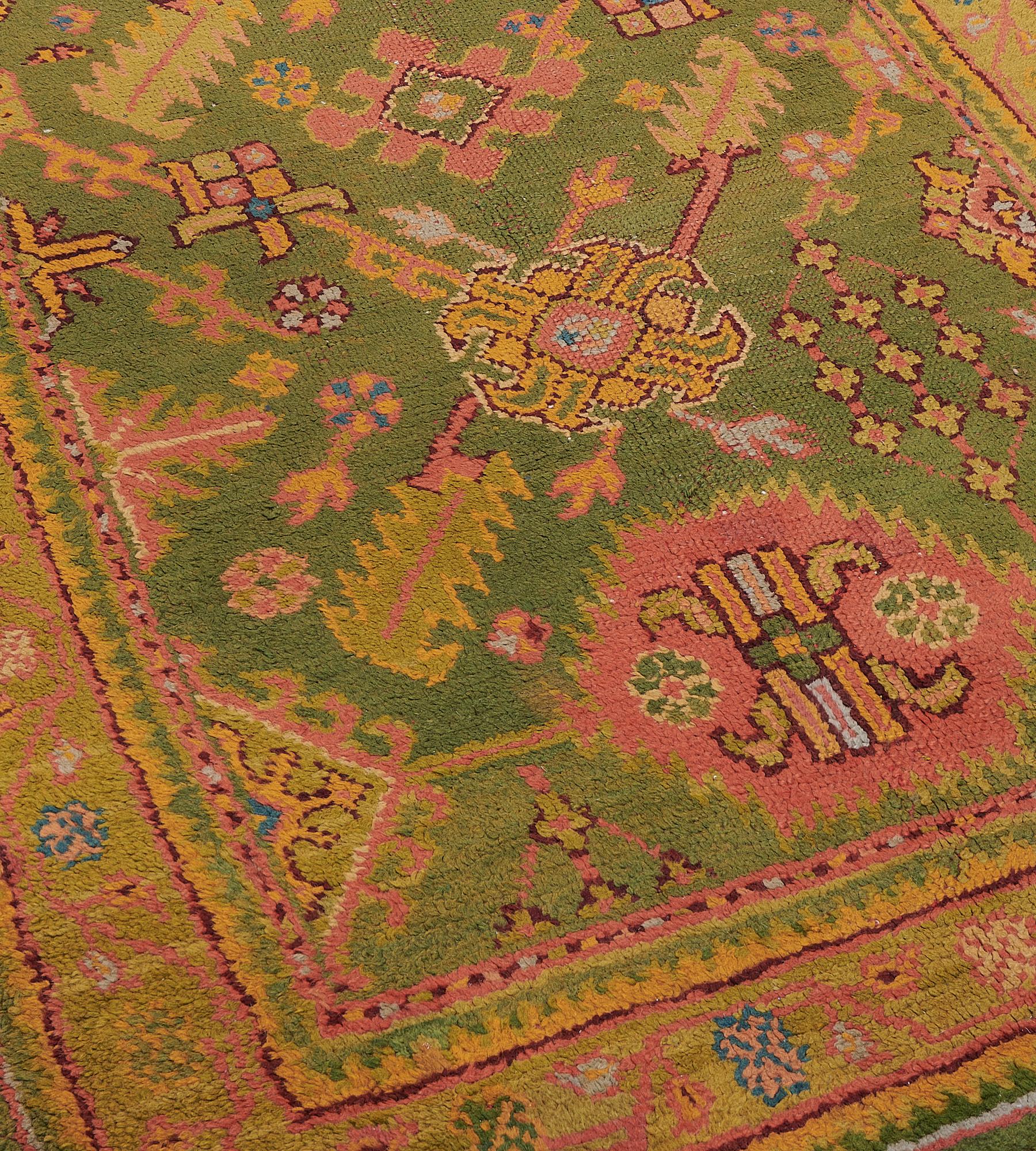 This antique, circa 1900, Oushak runner has an olive-green field with an central column of terracotta-pink serrated panels and pistachio-green hooked lozenges linked by angular serrated leaf vine, similar part lozenges and surrounded by floral