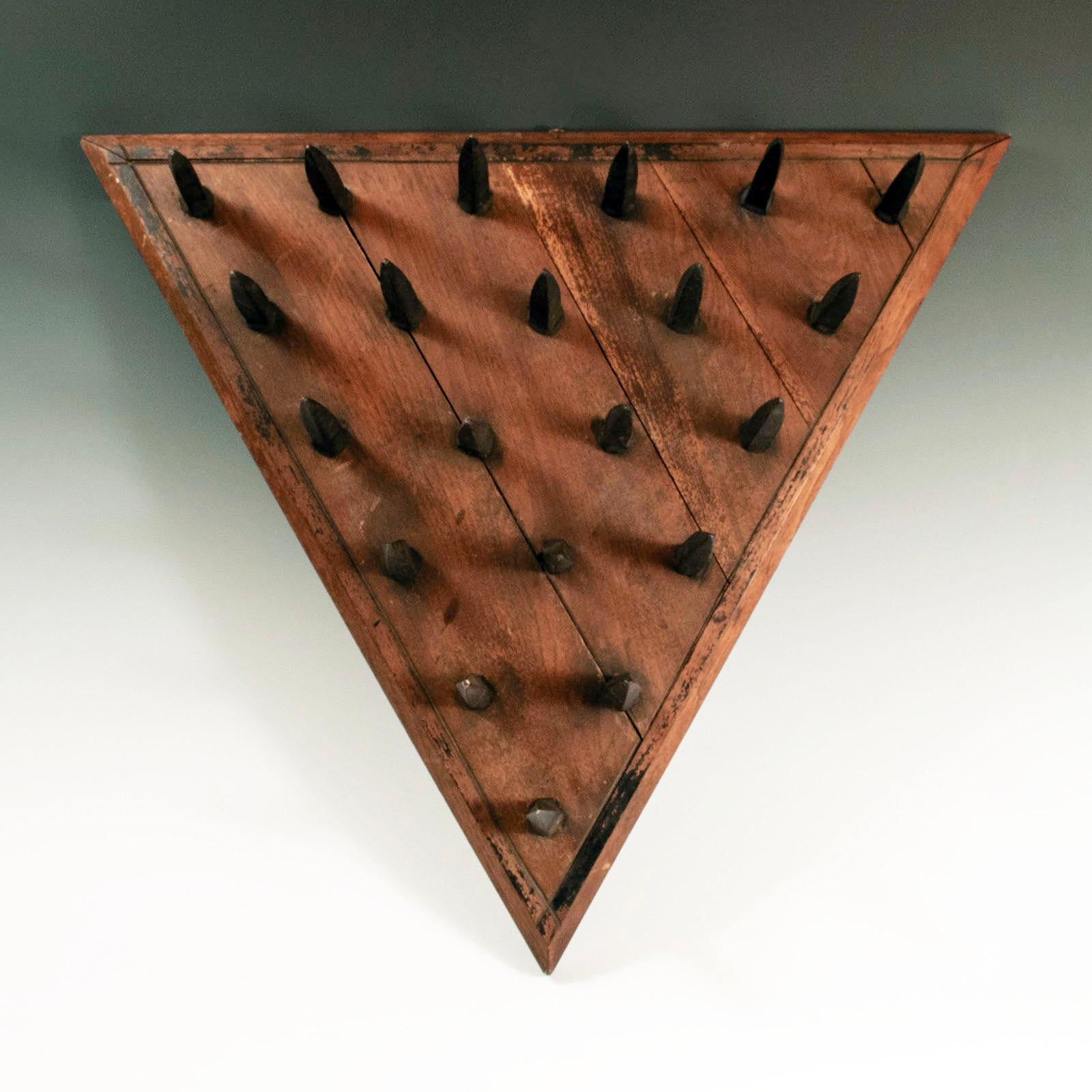 A rare triangular wooden seat studded with iron spikes, with remnants of black paint along the borders. During the initiation of new members, candidates were blindfolded after being shown a triangular chair with a seat of metal studs, such as this,