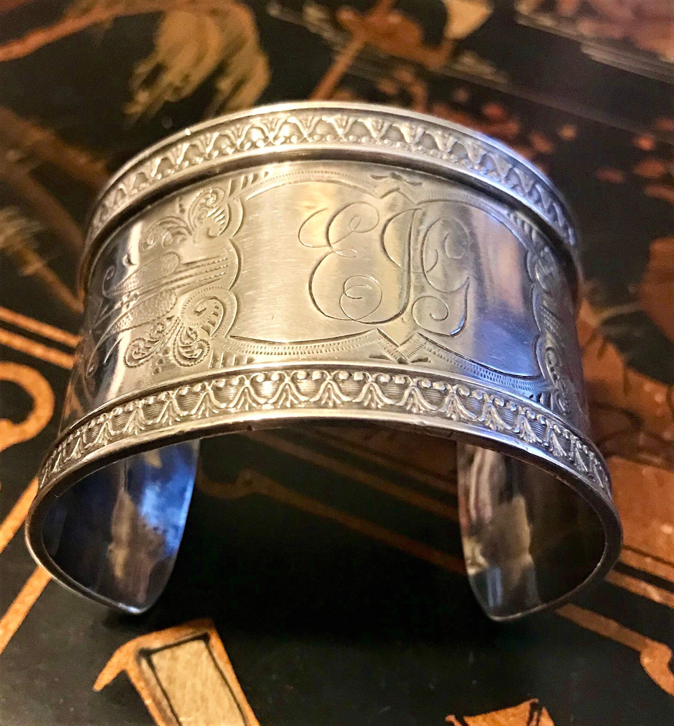 Circa 1900 sterling silver cuff bracelet with an engraved cartouche surrounded by an etched design.  The edges of the cuff are embellished with an ornate, raised sterling design and inside the cartouche is engraved with the initials EJG.   Inside