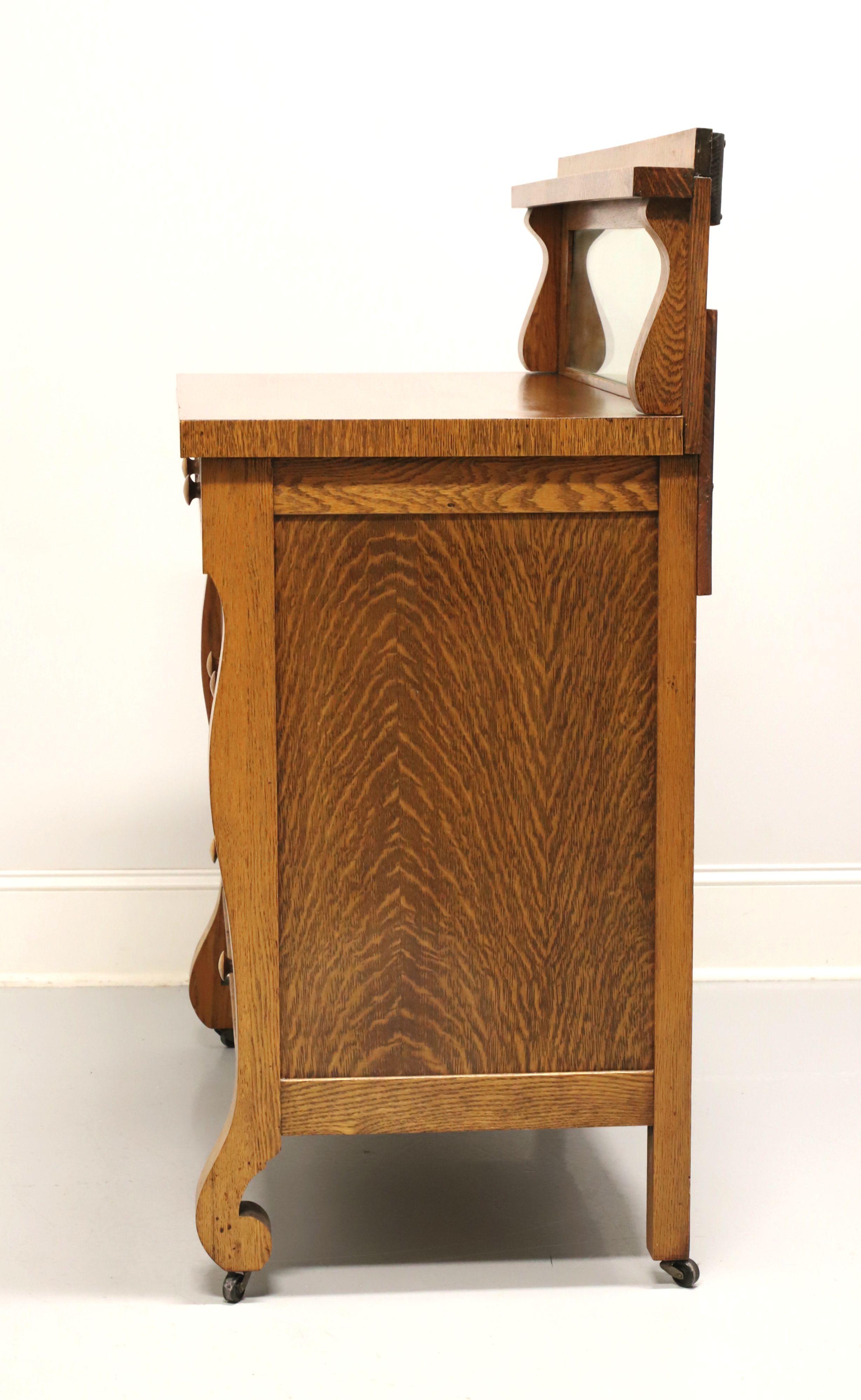 An antique circa 1900 Victorian era sideboard in the Empire style, unbranded. Tiger oak with wood knobs, upper gallery with mirror, curved front legs and on metal casters. Features a raised upper gallery with a rectangular mirror, three smaller