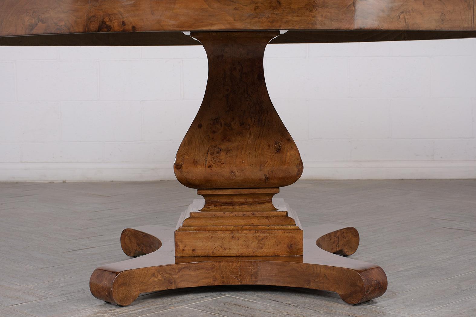 This 1900’s Empire-Style Burl Center Table has been completely restored and made of solid wood covered in a burl exotic veneers. This table features a beautiful inlay design and rests on a large carved pedestal base with scroll design feet. This