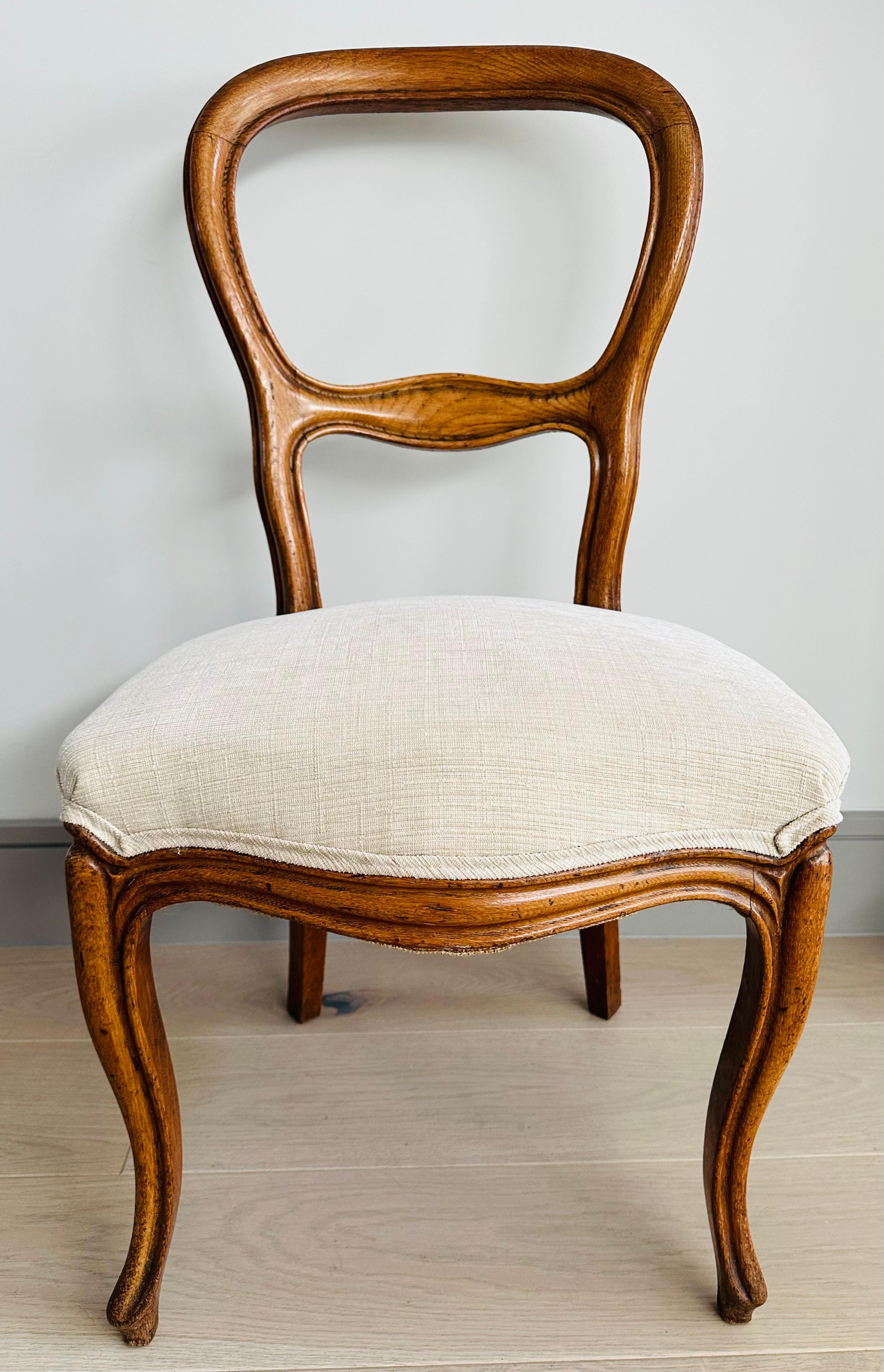 Circa 1900s oak balloon back side or dining chair which is characterised by its distinctive balloon-shaped back and simply carved around its border. The chair has turned legs and a newly reupholstered seat, making it both stylish and