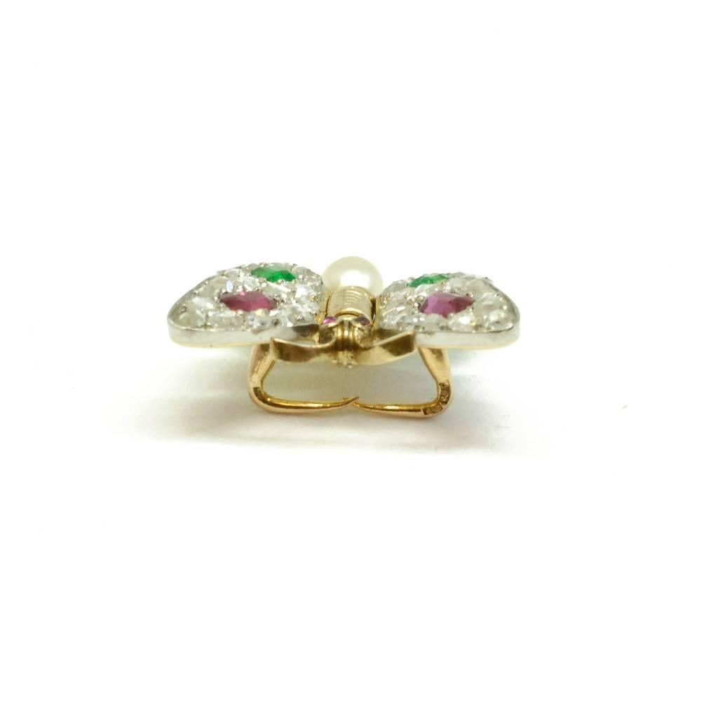 A rose diamond set butterfly pin, with moving wings set with rubies and emeralds, with a natural pearl set to the abdomen and ruby eyes. Mounted in 18ct yellow gold and platinum. French, circa 1905.

This piece is known as a 'flutter' pin, and is