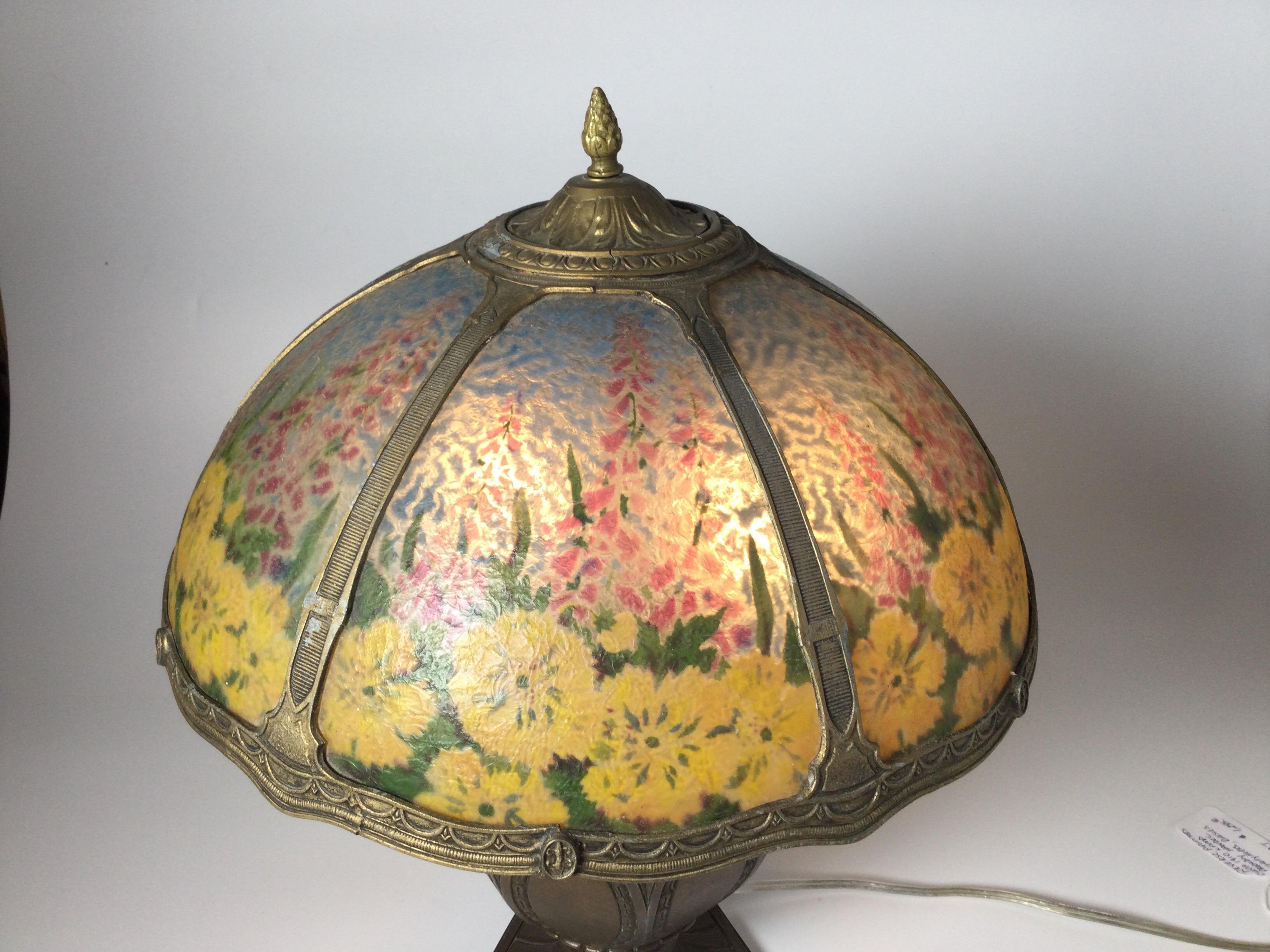 A hand reverse hand painted glass table lamp with bronze finish base, attributed to Handel, the painting depicts holly hocks, daisies on the shade. All original in beautiful original condition. No breaks to the glass, a few light and minor scuffs to
