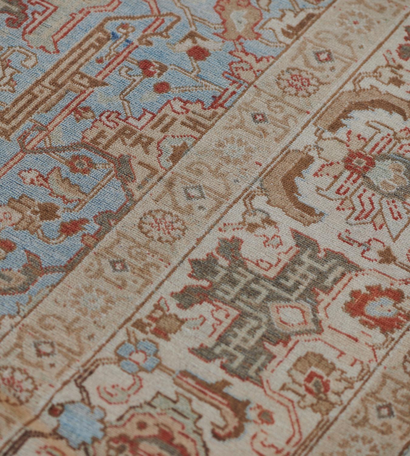 This antique, circa 1920, Tabriz rug has a light blue field with an overall design of light grey and ivory angular floral and leafy vine and brick-red and shaded chocolate-brown part palmettes, in a broad ivory border with ivory and light blue