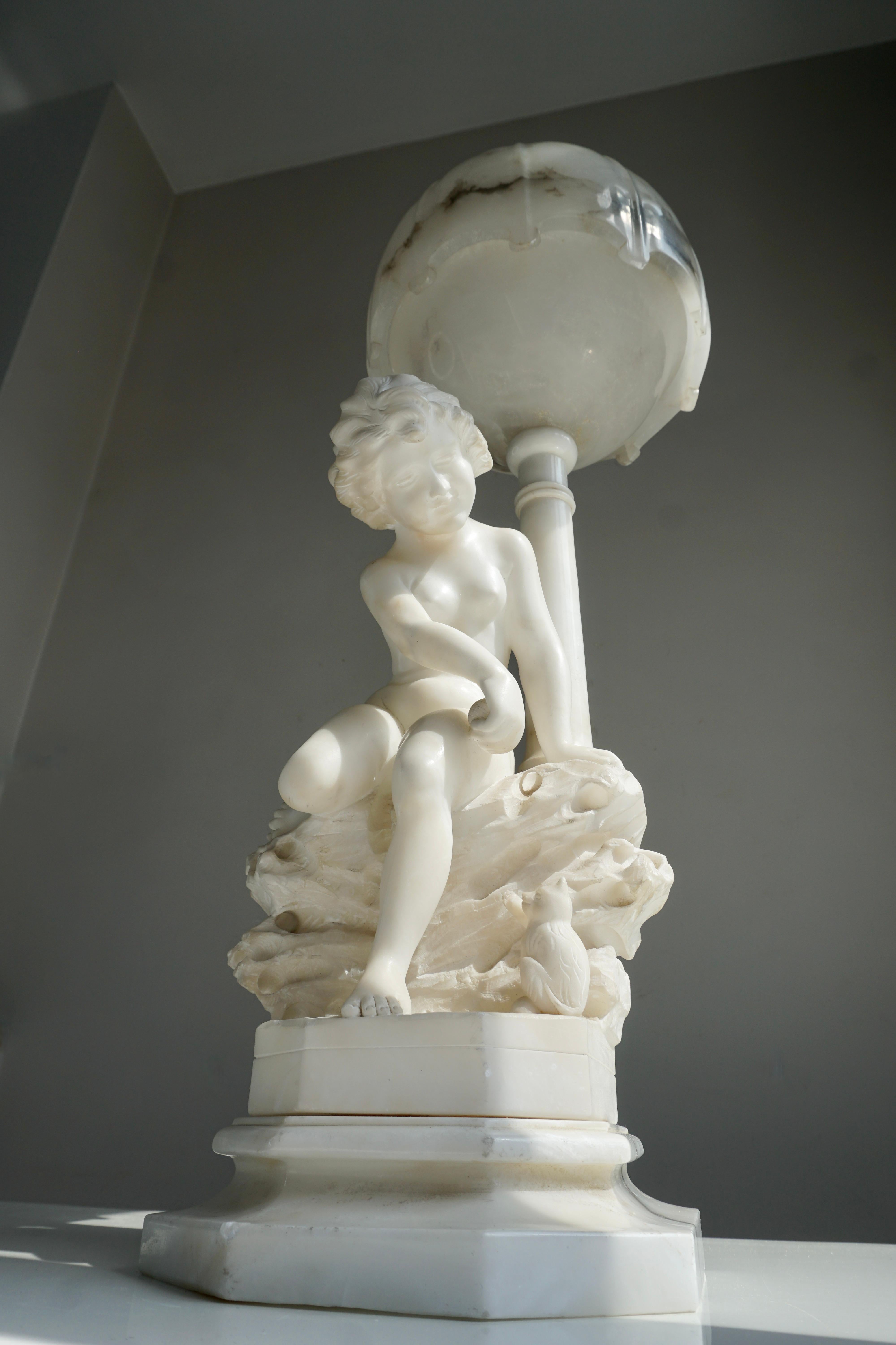 Fine rare antique Italian alabaster lamp depicting a beautiful young girl sitting on a rock , playing with a kitty cat. The shade is a 2-piece globe, also made of alabaster.

This Circa 1920 hand-carved alabaster lamp serves as both an art form as