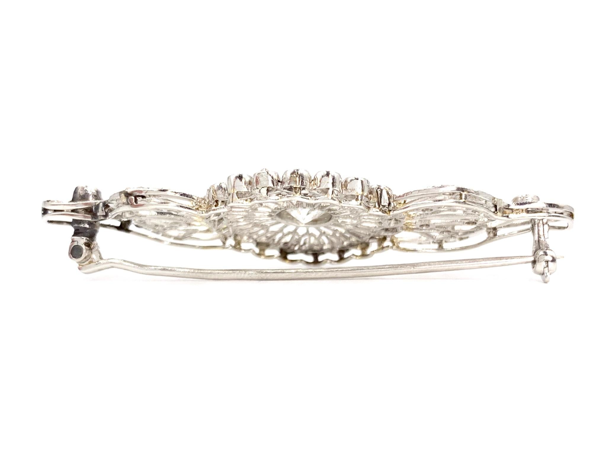 Made with fine craftsmanship with an airy feminine style, this 14 karat white gold Edwardian style diamond brooch showcases a center Old European cut white diamond, weighing approximately .80 carats at approximately G color, SI1 clarity. Center