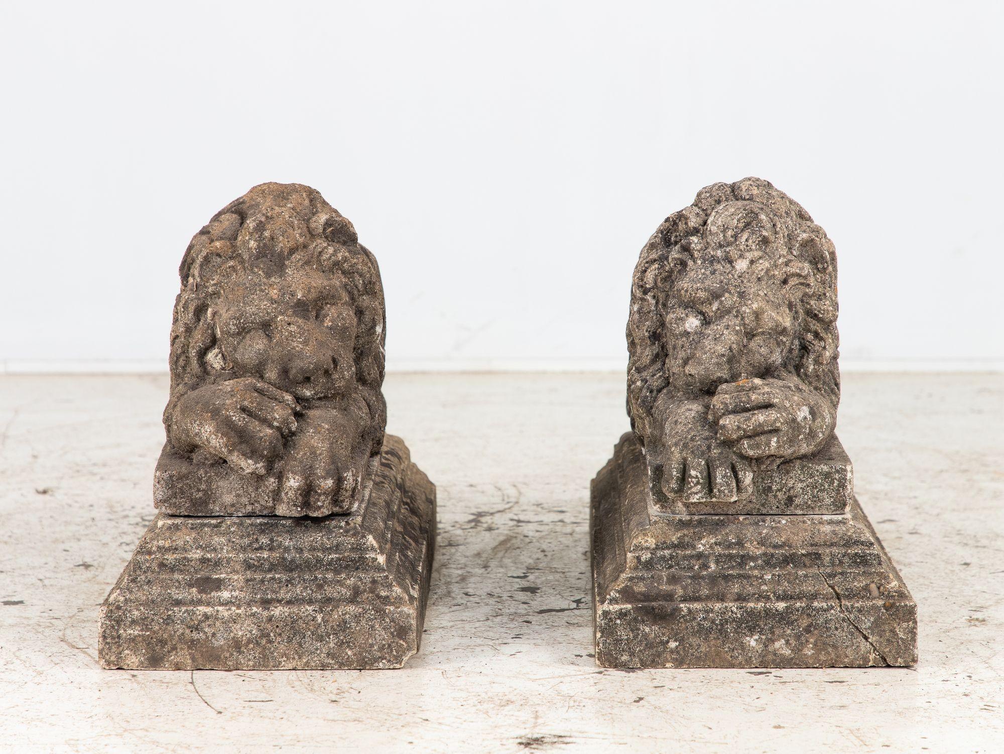 This pair of circa 1920 English recumbent lions is crafted from weathered concrete with finely detailed features, from flowing manes and curled tails to expressive, carved faces and powerful paws. Measuring 13