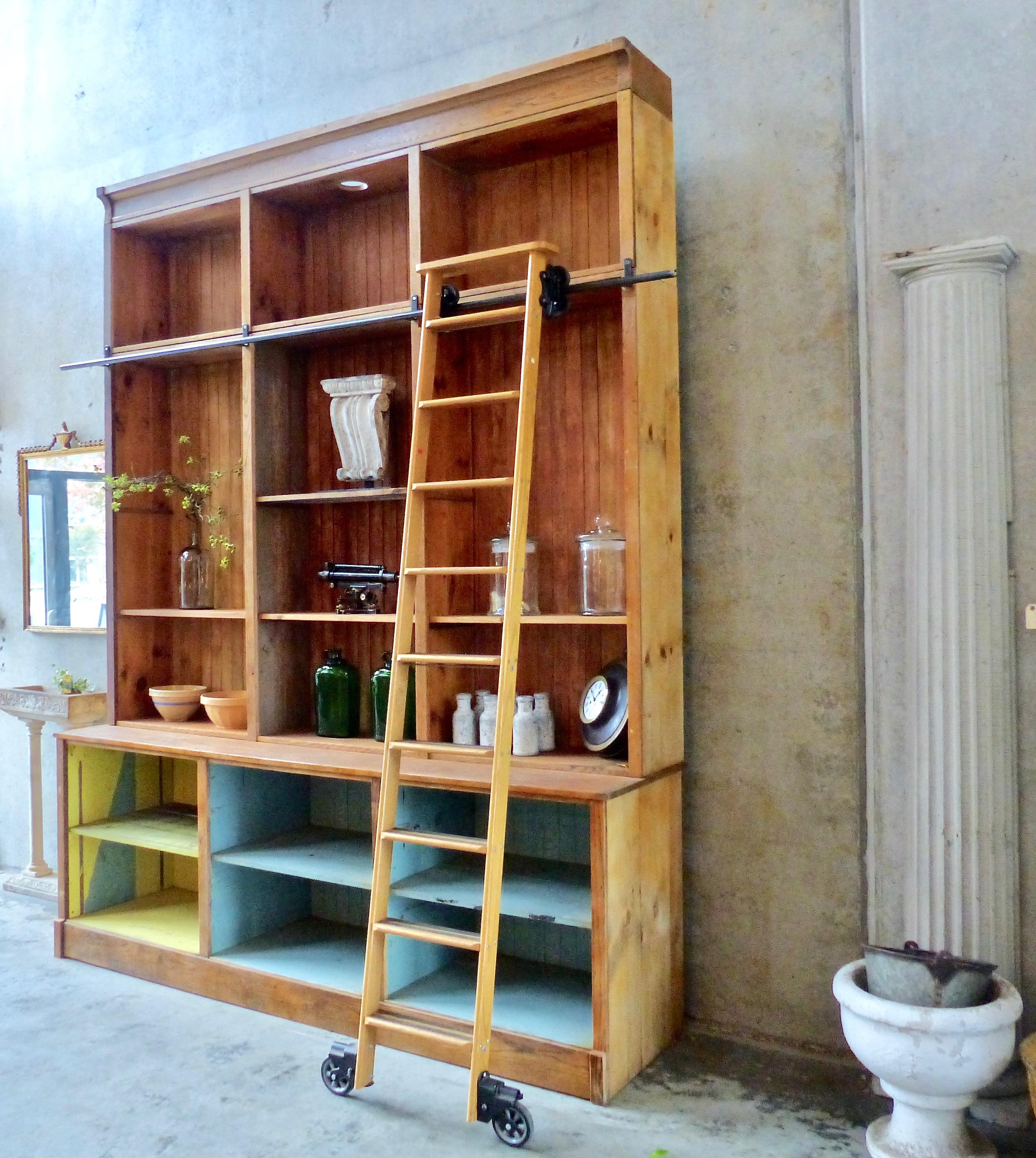 Salvaged from a former hardware store, a circa 1920 pine storage unit. Comes complete with a rolling library-style ladder, and features multiple open shelves backed by bead board. The large cabinet breaks down into components for ease of shipping