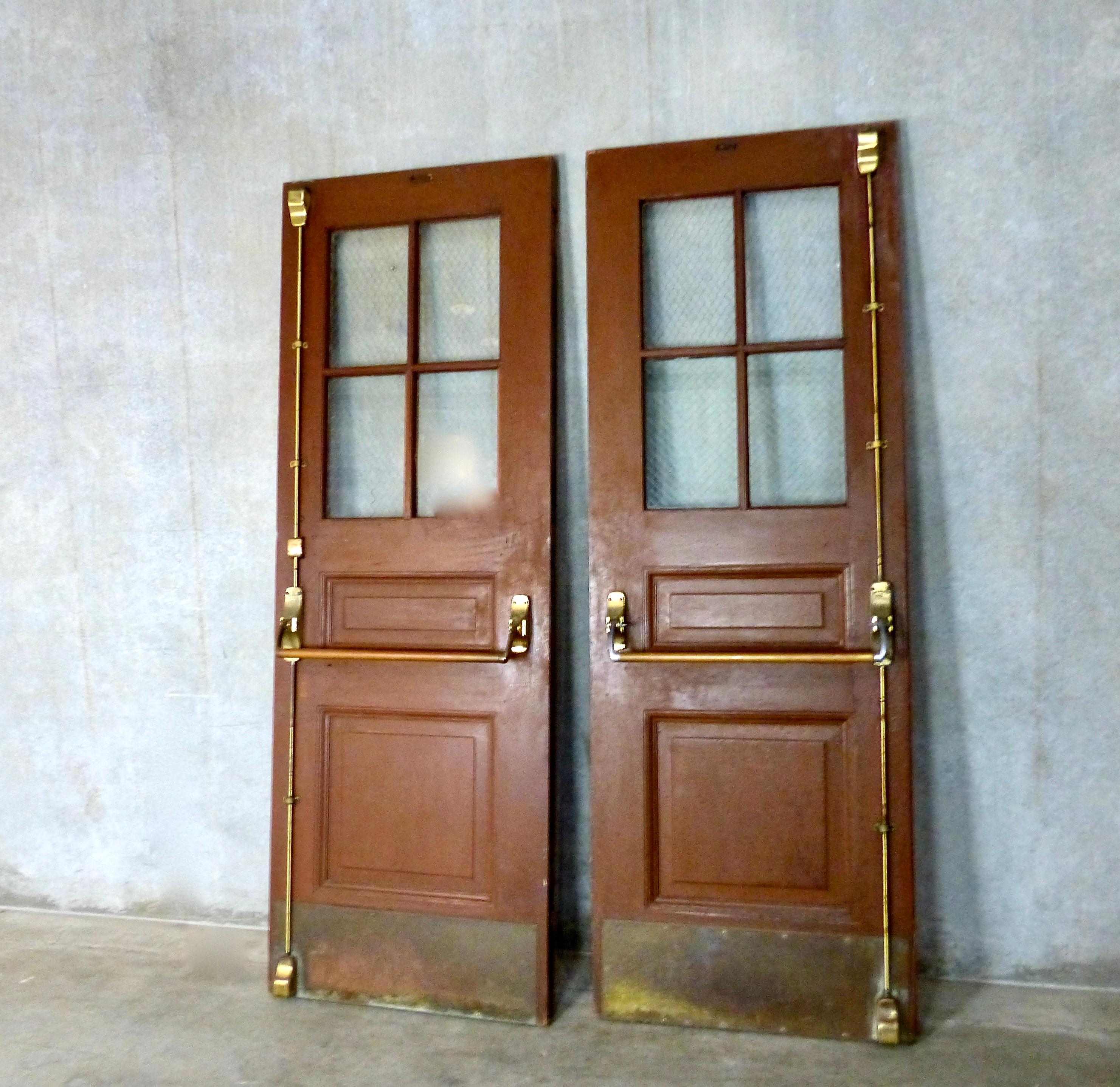 A circa 1920 matched pair of beautiful solid oak exterior doors — outfitted with commercial-style brass push bars and kick plates. Includes original brass hardware (doors handles, hinges, etc.) as well as authentic chicken wire glass in each of the