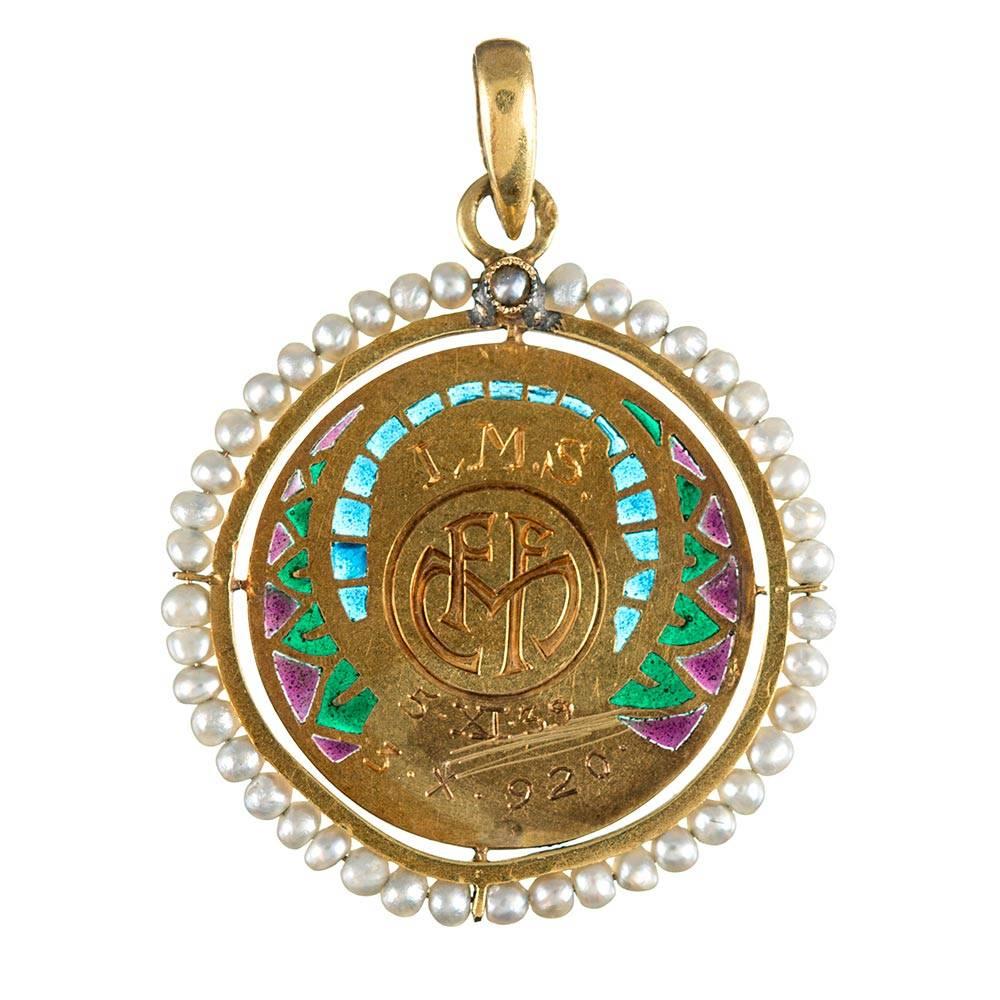 Measuring just over 1 inch in diameter, this sweet pendant is hand made of 18 karat yellow gold, decorated with a purple, green and blue “plique-a-jour” enamel and framed in a border of natural seed pearls. Note the immense detail achieved in the