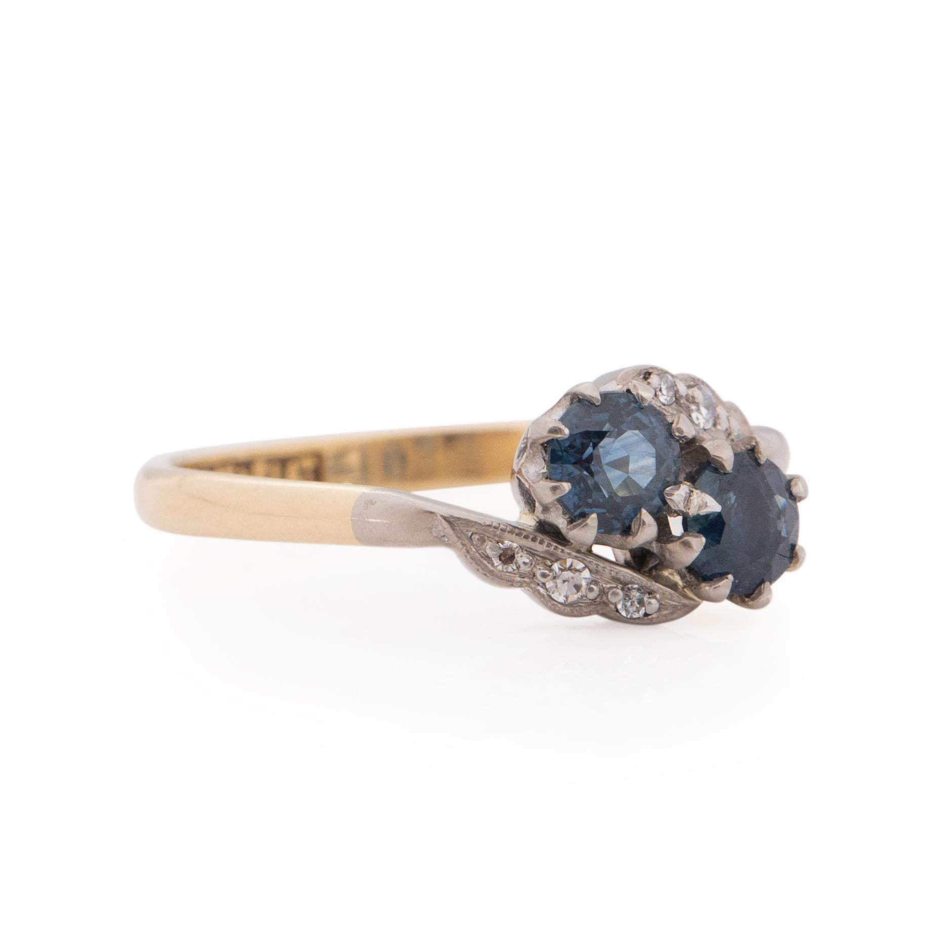 Here we have a beautiful art deco bypass style ring. In the center are two blue jean colored sapphires, the hue is not something that is come by all that often. Holding the sapphires is a classic prong setting. On either side of the center gems are