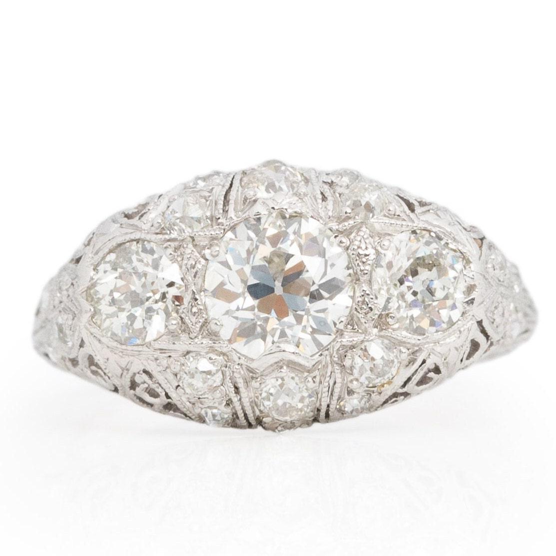 Presenting an exquisite Art Deco masterpiece, meticulously crafted in platinum. This three-stone ring boasts exceptional filigree intricacies, with lace-like patterns delicately embracing the diamonds, creating an ethereal effect. At its heart lies