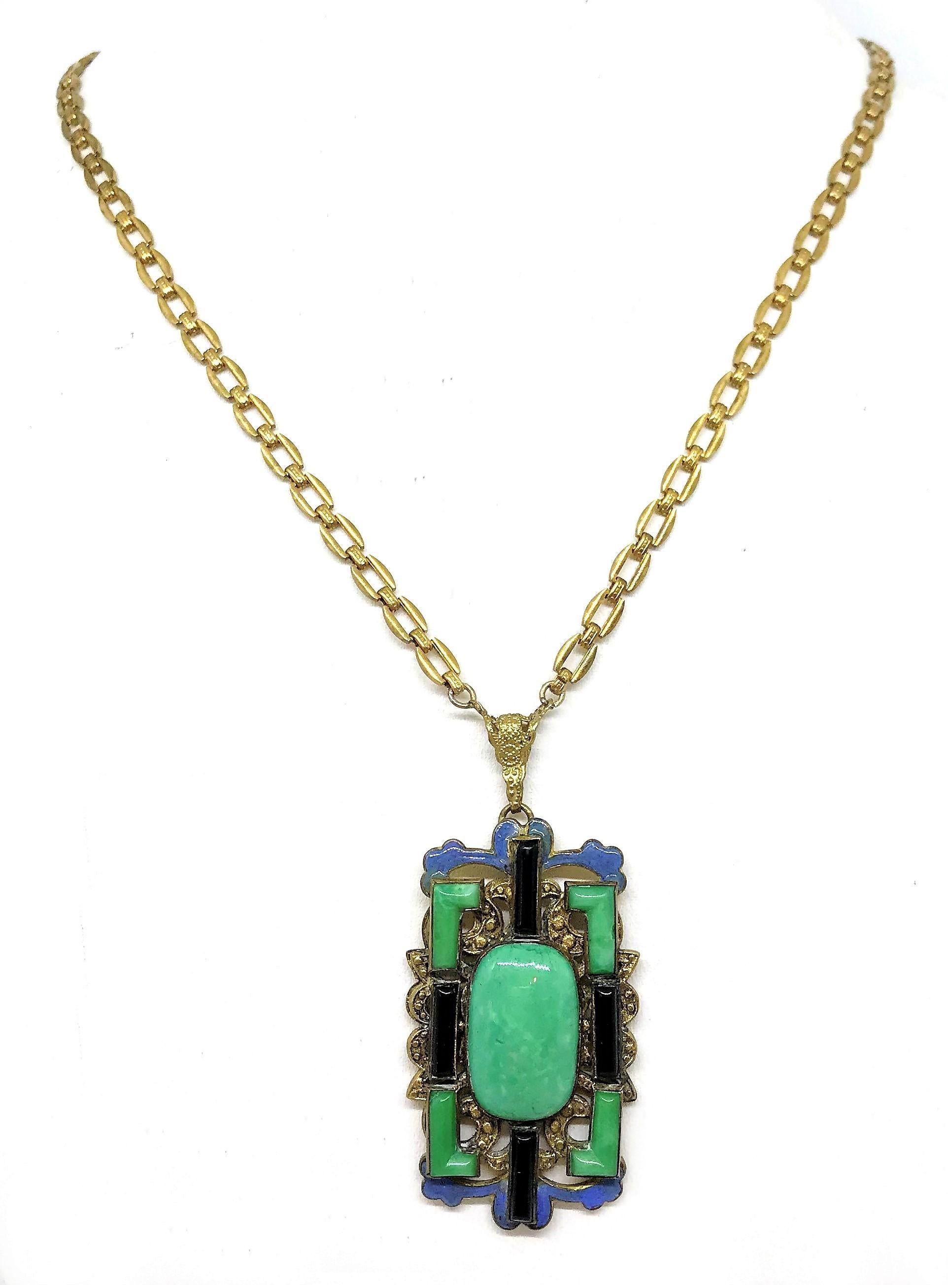 Circa 1920s Czech chain necklace with an ornate brass pendant, bezel set with an oval green glass cabochon and embellished with bezel set green and black molded glass stones and blue enameling.   The necklace measures 19