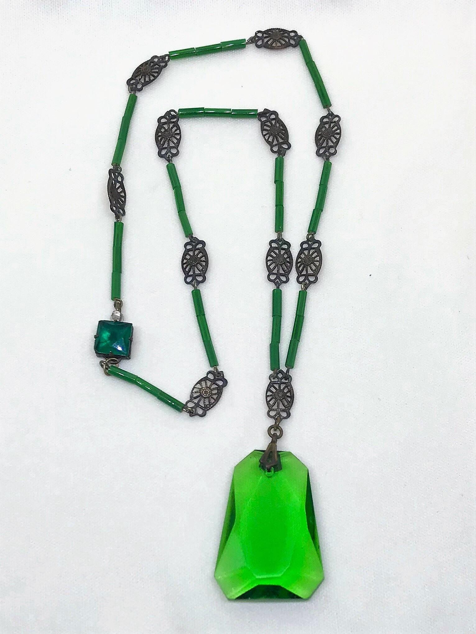 Circa 1920s necklace of green glass tube beads interspaced with ornate brass links hung with a green faceted glass pendant.  It measures 17