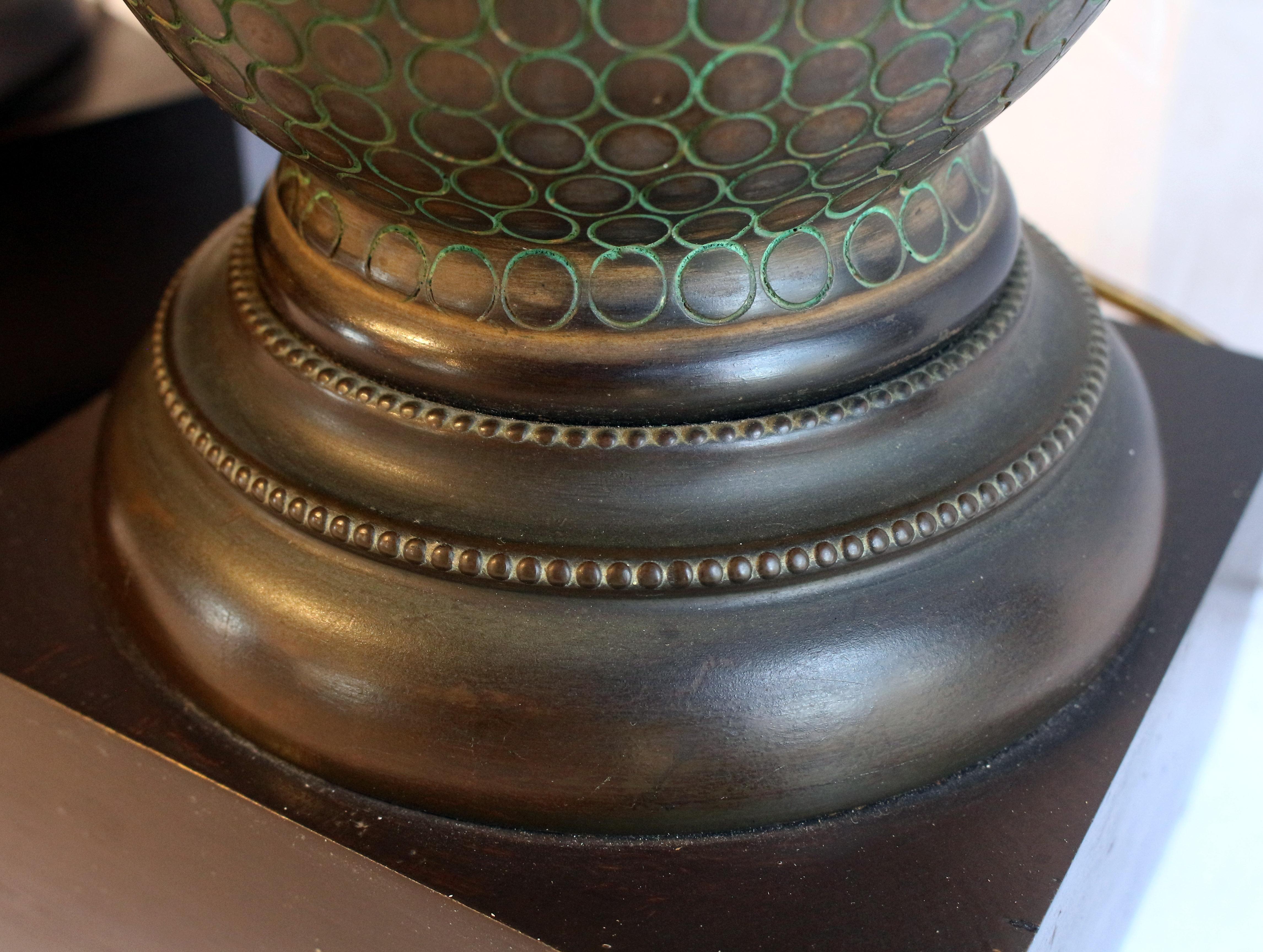 Vers 1920, paire de lampes en bronze de forme vasculaire sur des bases carrées en bois, probablement américaines. Les formes des vases sont recouvertes d'un motif de cercles éternels compensés par une patine vert-de-gris ; les bases en bronze