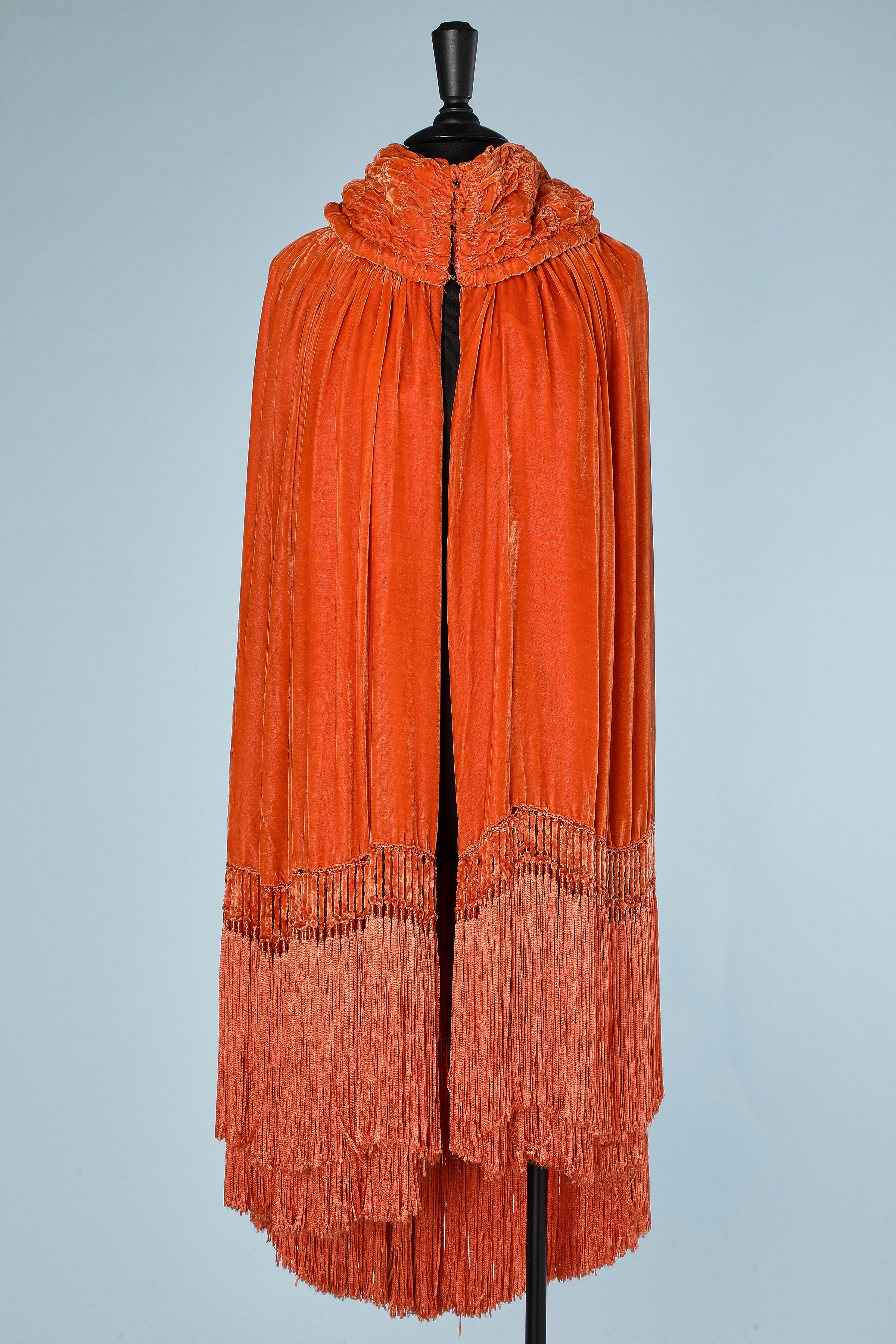 Circa 1920's Opera cape in orange silk velvet and silk &velvet fringe.
Arms opening inside the cape but hidden. Double lays of velvet and fringes in the back. The collar is fully ruffled. Orange silk lining very damaged. Sort of scarf in the middle