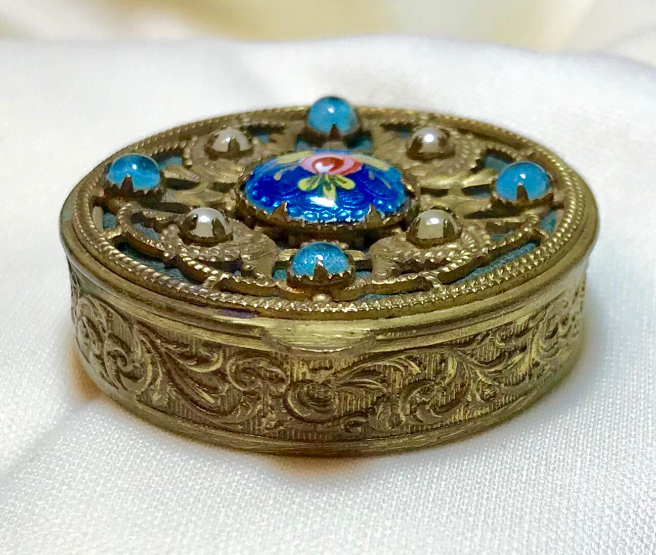 Circa 1920s French ornately designed gold tone powder compact. The top has an openwork design over a blue-green fabric and is embellished with prong set glass cabochons around a guilloche enamel cartouche with a hand painted rose.  It is decorated