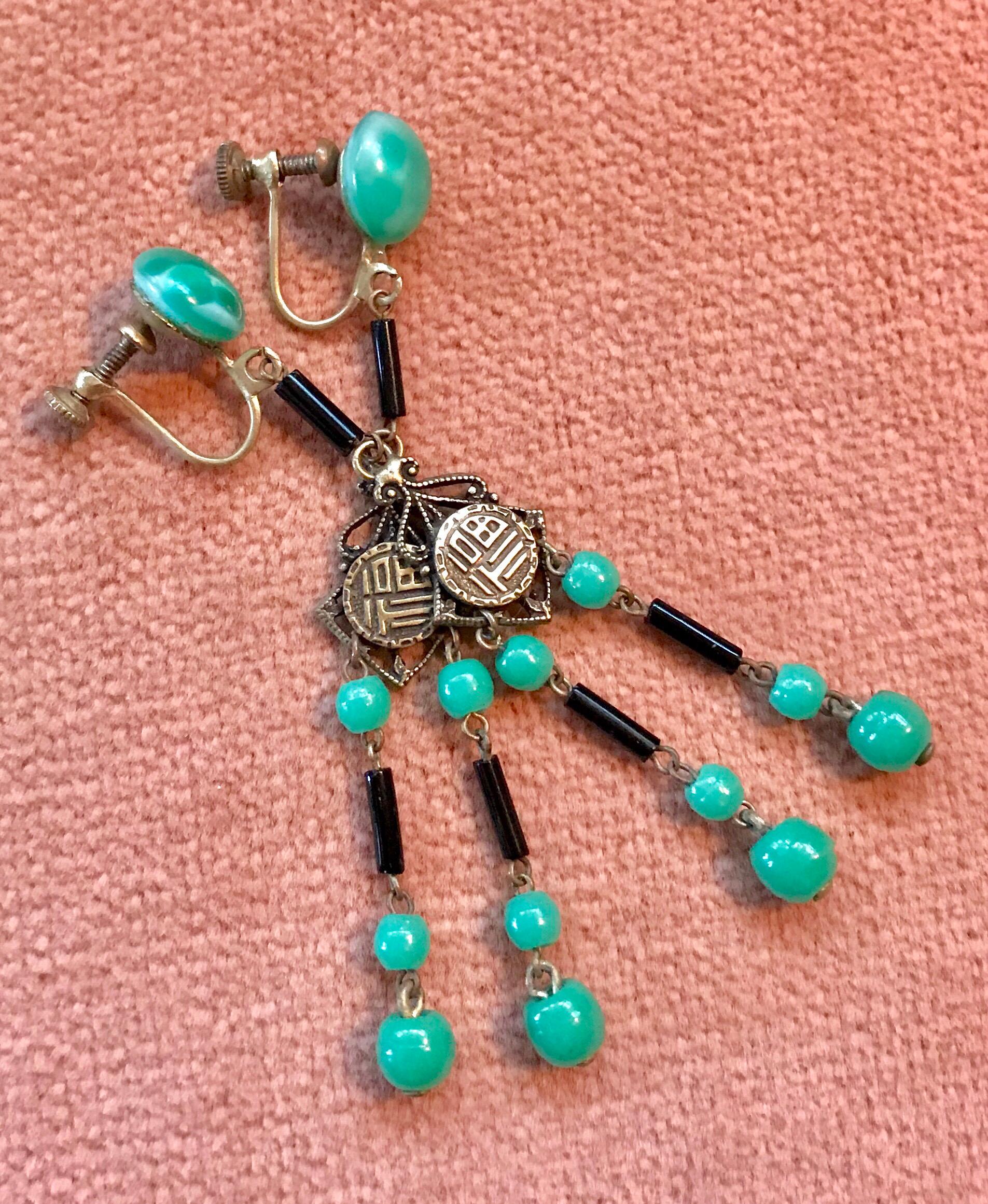 Circa 1920s Art Deco screw back, dangling earrings with a green glass cabochon top.  They are embellished with brass decorative plaques, green round beads and black glass tube beads.  Each earring measures 2.7