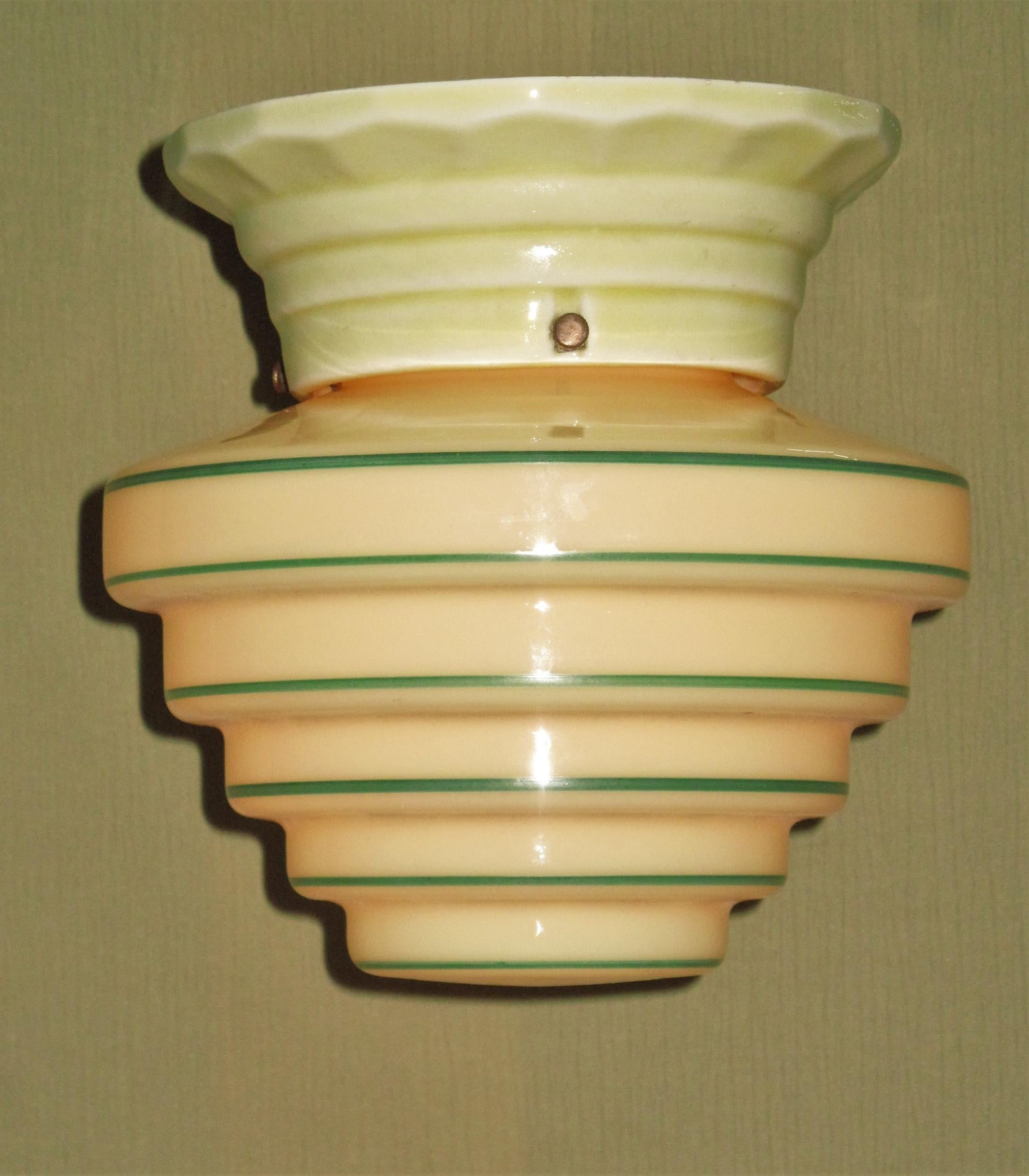 From the late 20s or early 30s is a wonderful marriage of a custard McBeth Cremax globe on a yellow porcelain ceiling fitter. Both pieces are in excellent condition with no cracks or noticeable chips. The green strips on the globe, which are fired