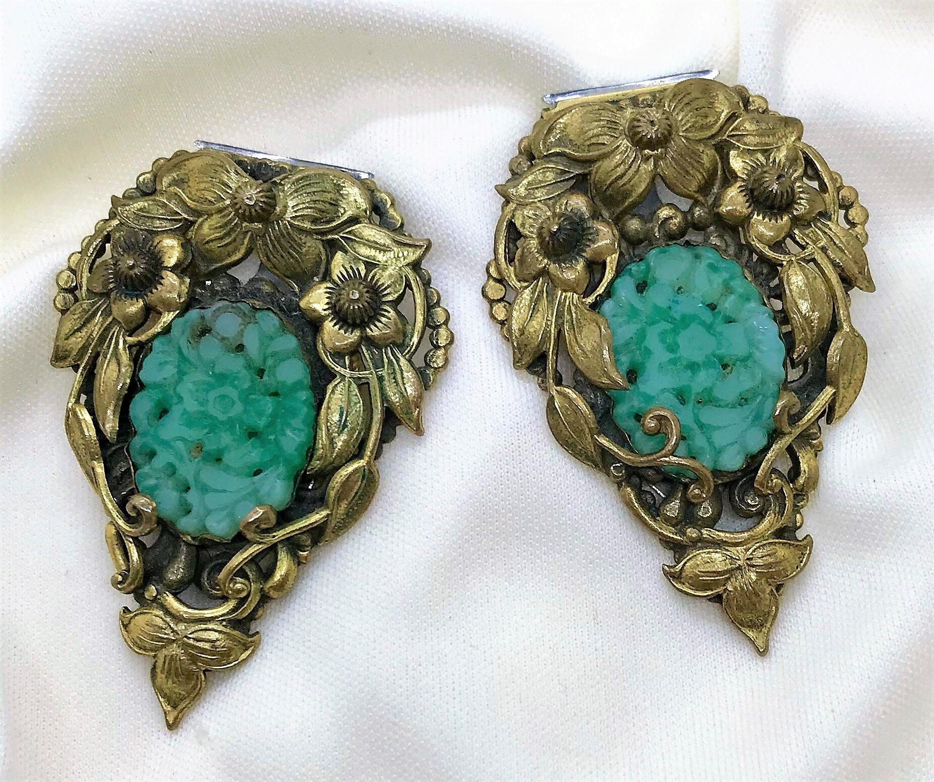 Circa late 1920s to early 1930s pair of plated brass dress clips done in an ornate, floral motif and set with molded jade green glass ovals.  Each dress clip measures 2.1