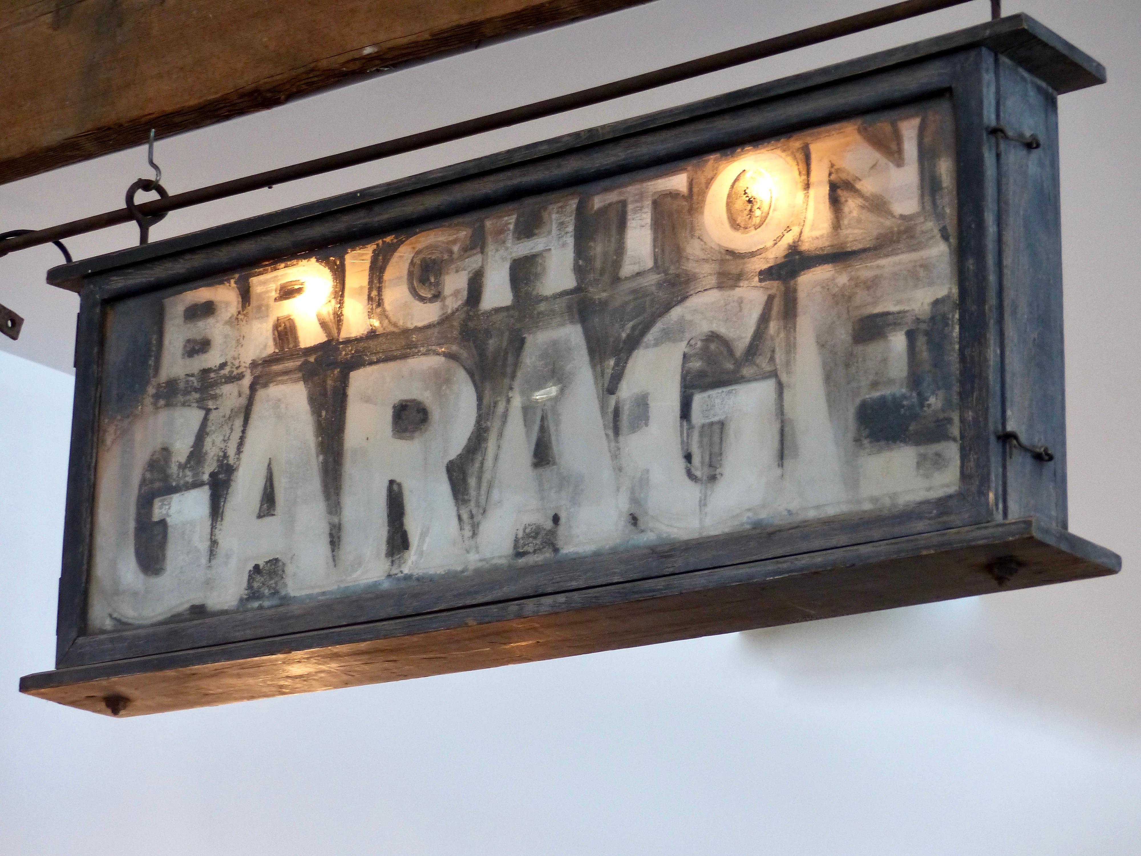 This is a very rare one of a kind automotive collector item.
Cantilevered cast iron sign for Brighton Garage. Two-sided, electrified sign with its lettering reverse-painted on glass. Wall-mounted mechanism, in wrought iron, for displaying the sign