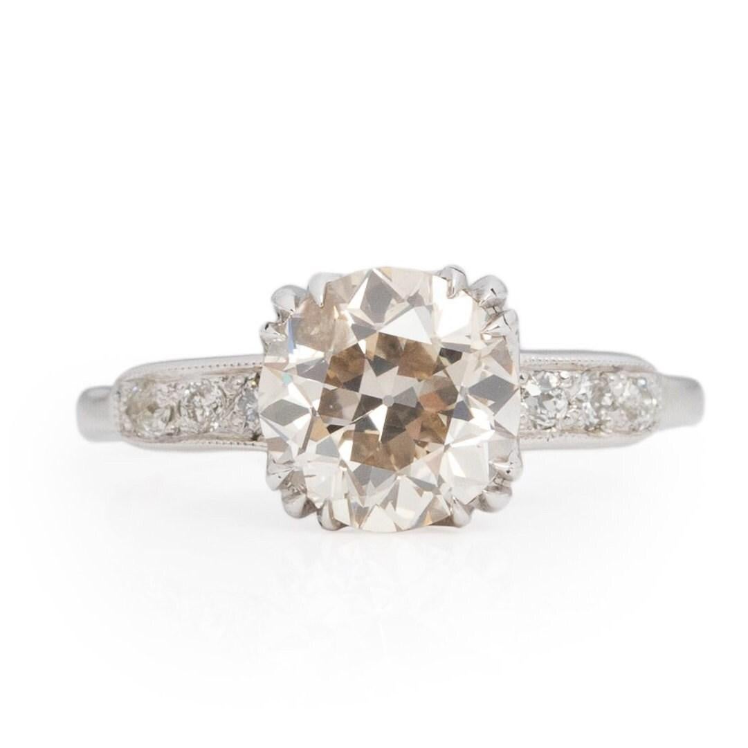 Presenting an enduring symbol of elegance, this Art Deco engagement ring crafted from 18K white gold exudes timeless allure. The sleek, straight shanks gracefully lead the gaze towards a trio of single-cut diamonds adorning the shoulders. Delicately