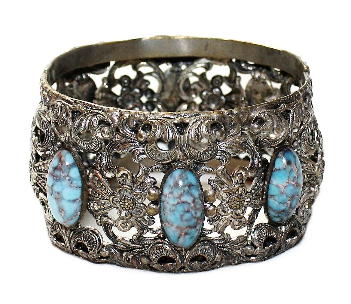 Circa 1930s to 1940s silver-plated brass hinged bangle with an ornate floral motif.  The bracelet is bezel with six oval faux-turquoise glass stones.  It measures 2.25