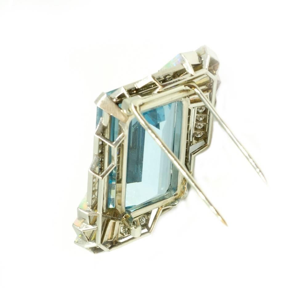 An aquamarine and white opal dress clip of asymmetric design by Yard. Four tapered slivers of opal are set into two diagonally opposing corners with two rows of diamond running up each side of the emerald cut aquamarine. Mounted in platinum.