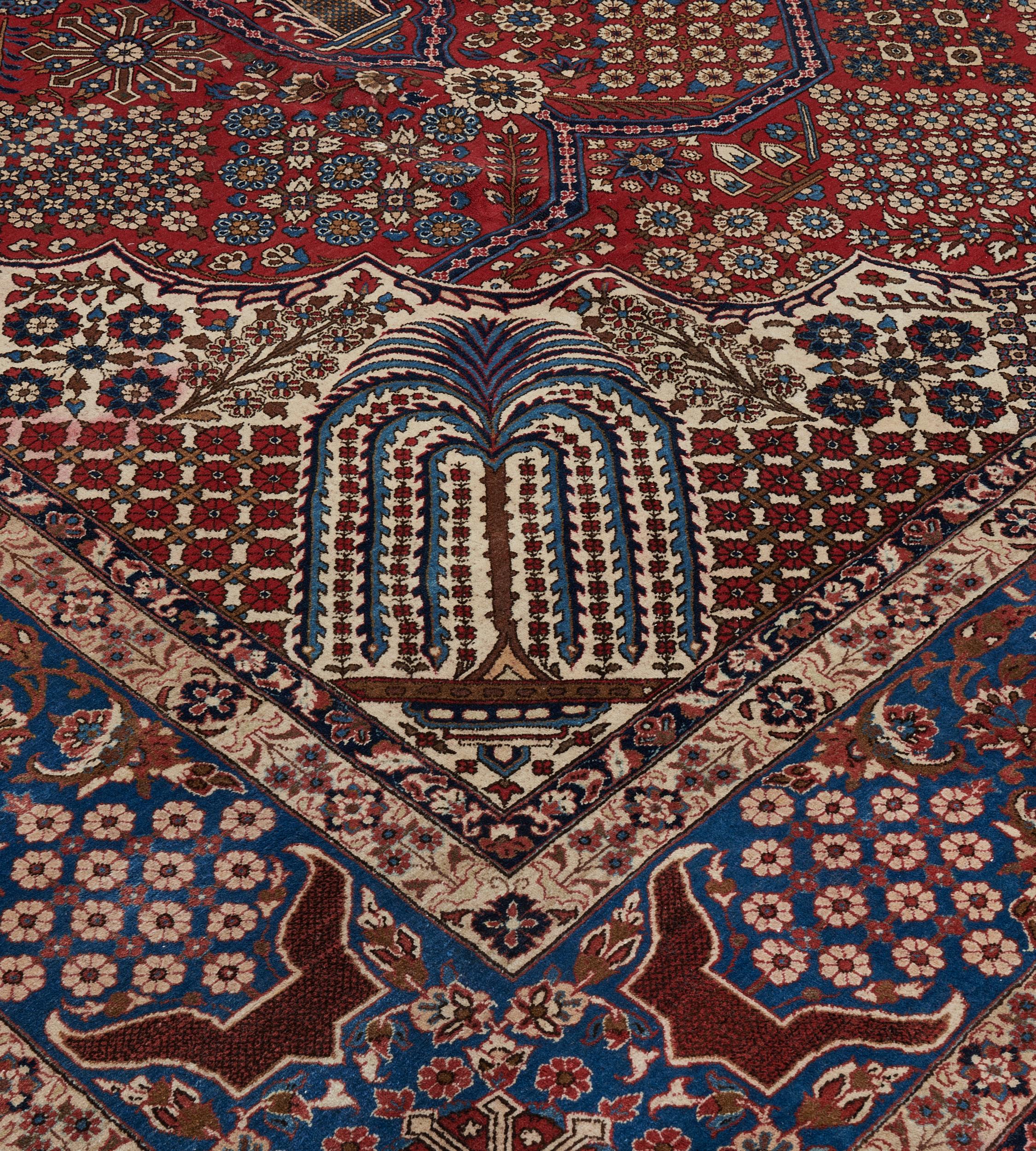 This traditional, circa 1940, hand-woven Persian Isfahan has a tomato-red field with a central indigo-blue cusped medallion with palmette pendants containing a dense profusion of flowerheads and a pair of weeping willows surrounded by open lozenges