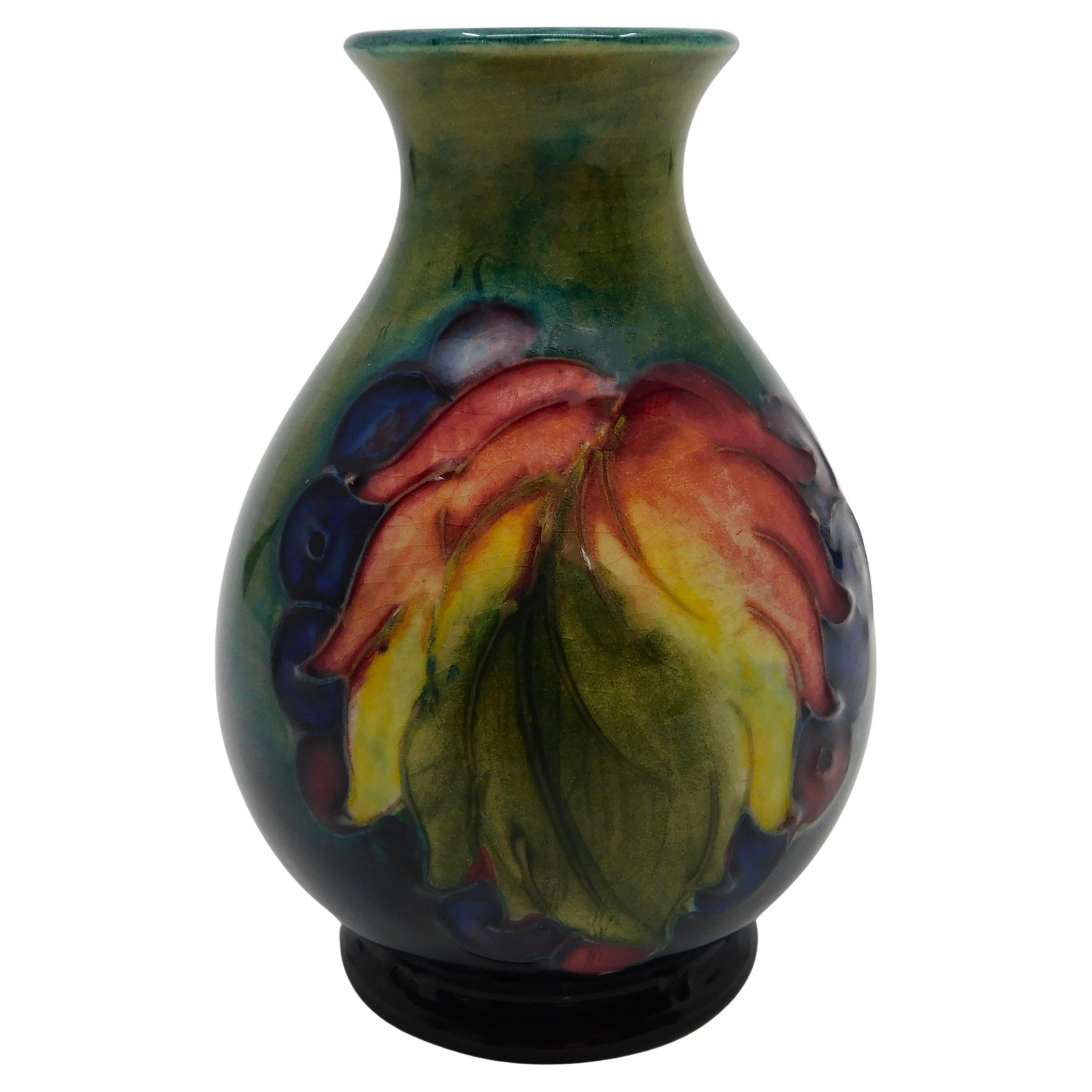 This beautiful art pottery vase was done by the Moorcroft Pottery company of England in circa 1940 using their signature deep cobalt blue ground and done in the 'Leaf and Berry' pattern.  Designed and produced by William Moorcroft It features fine