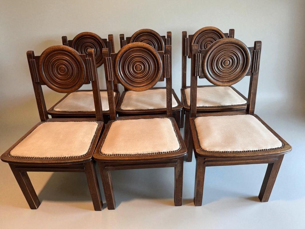 This striking set of six dining chairs pays tribute to the bold, architectural vision of Charles Dudouyt, a celebrated figure of French decorative arts in the 1930s and 1940s. Crafted from solid dark-stained oak, each chair features a sculptural