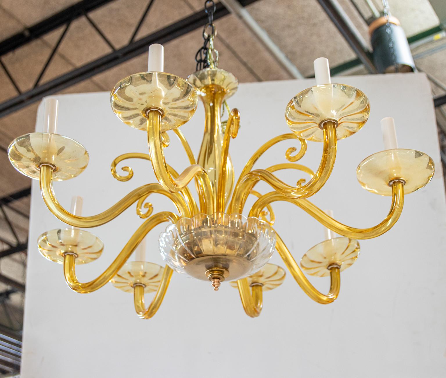 Circa 1940s large murano glass chandelier in an amber hue with glass bobeches. The chandelier is further detailed with scrolled glass accents and a glass dome finial at the base with scalloped trim. Please note of wear consistent with age. Shades