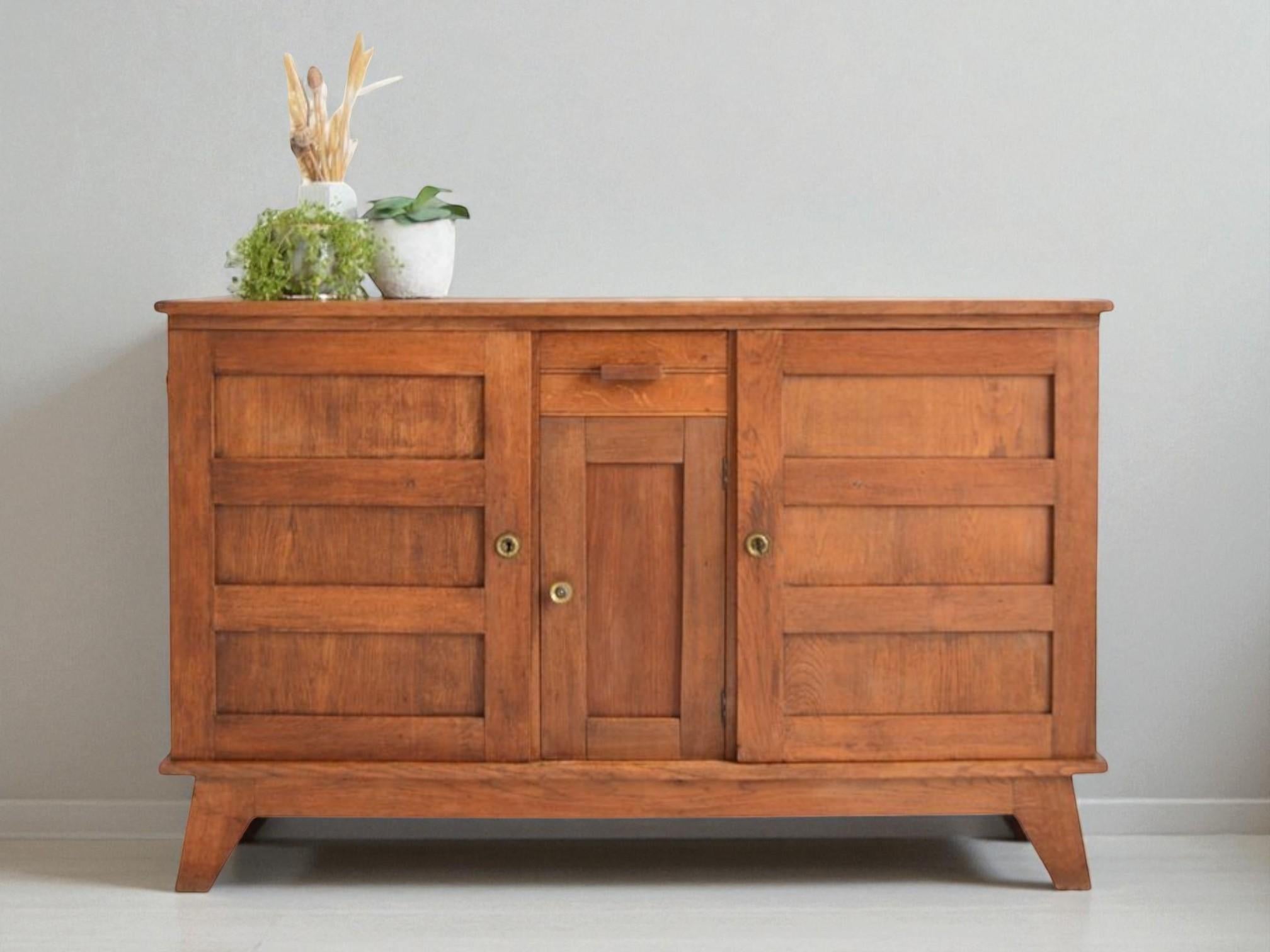 This minimalist yet sturdy sideboard exemplifies the clean lines and functional elegance of French post-war modernist design. Crafted from solid oak, the piece features a simple, rectilinear structure softened by a warm, medium-toned finish that