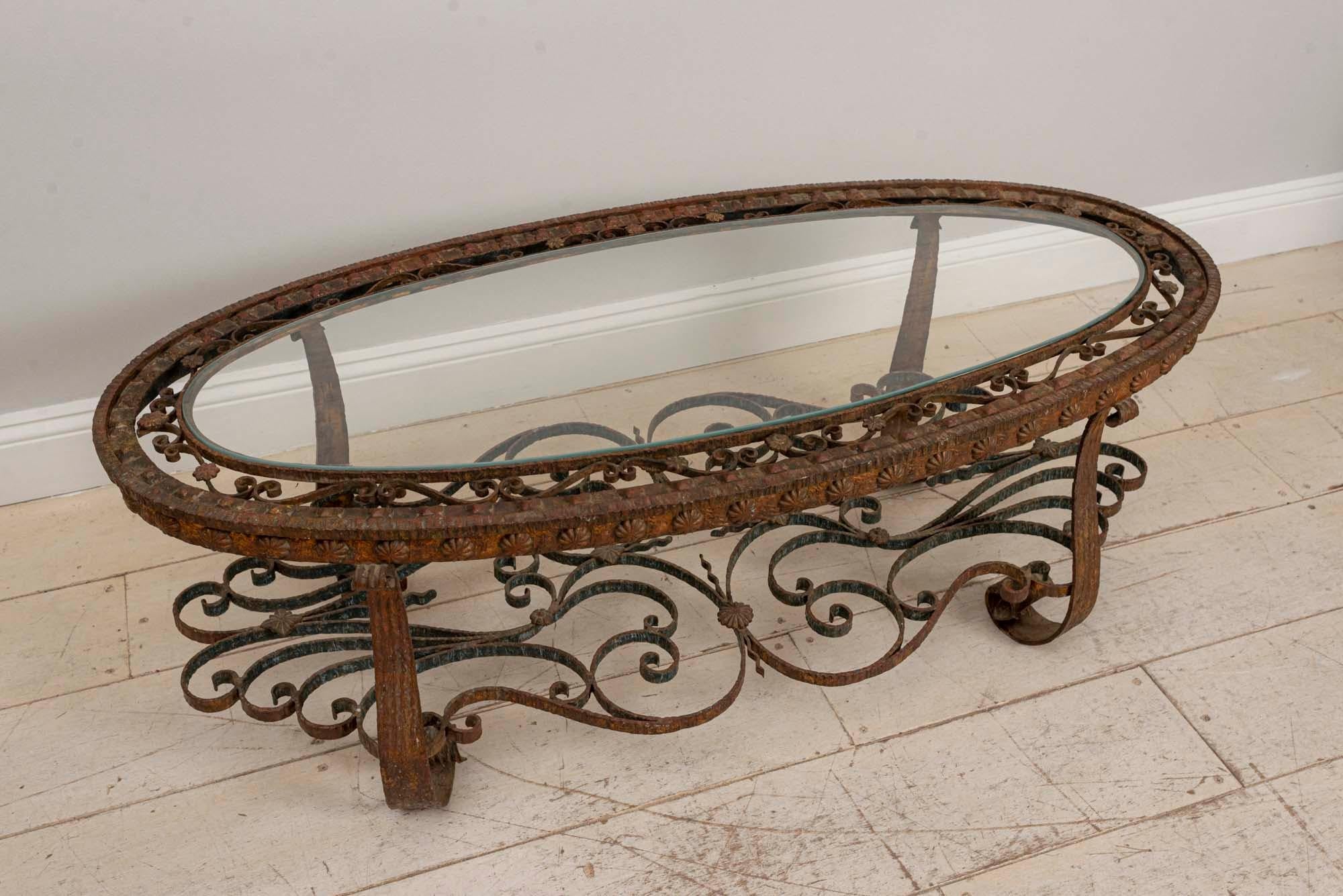 A stunning and extremely decorative oval-shaped coffee table made from wrought iron. The table top features a toughened glass oval shaped top which is inserted into scrolled wrought iron detail around the perimeter which holds it in place. The shelf